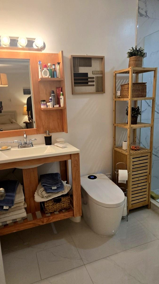 Bathroom featuring an open-shelf wood vanity with a white countertop and integrated sink, a multi-bulb vanity light, and large-format tile flooring