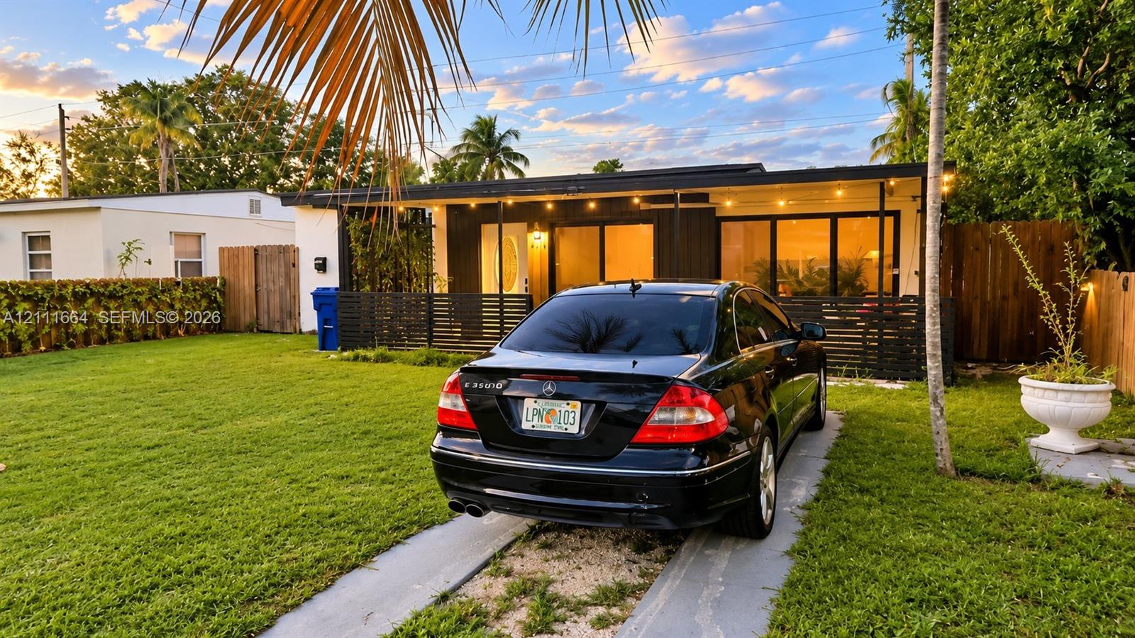 Single-story exterior featuring a covered front porch, dark-toned horizontal slat fencing, integrated exterior lighting, and a concrete ribbon driveway