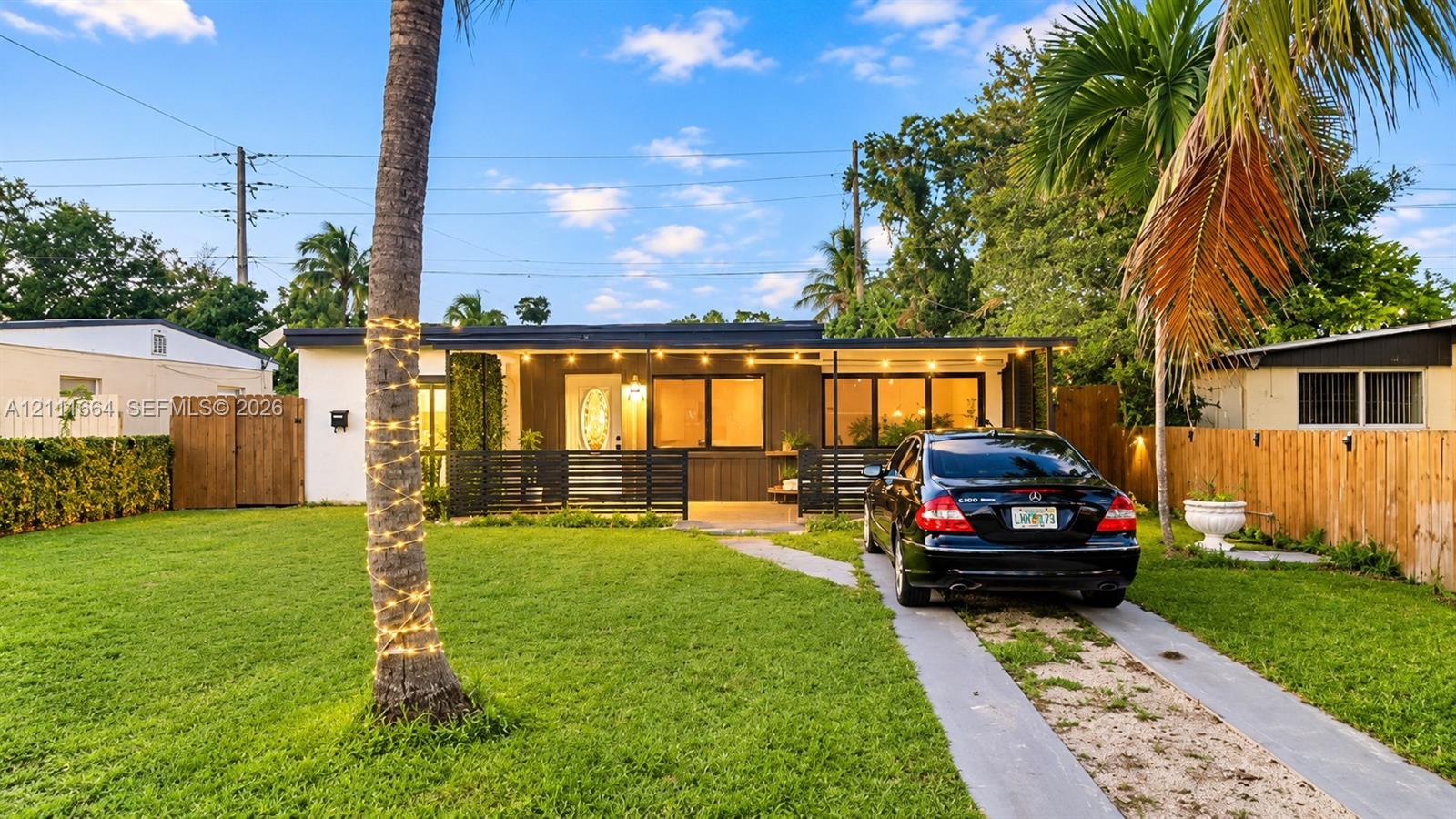 Single-story exterior featuring a covered front porch, horizontal wood-panel siding, mature palm trees, and a concrete-strip driveway