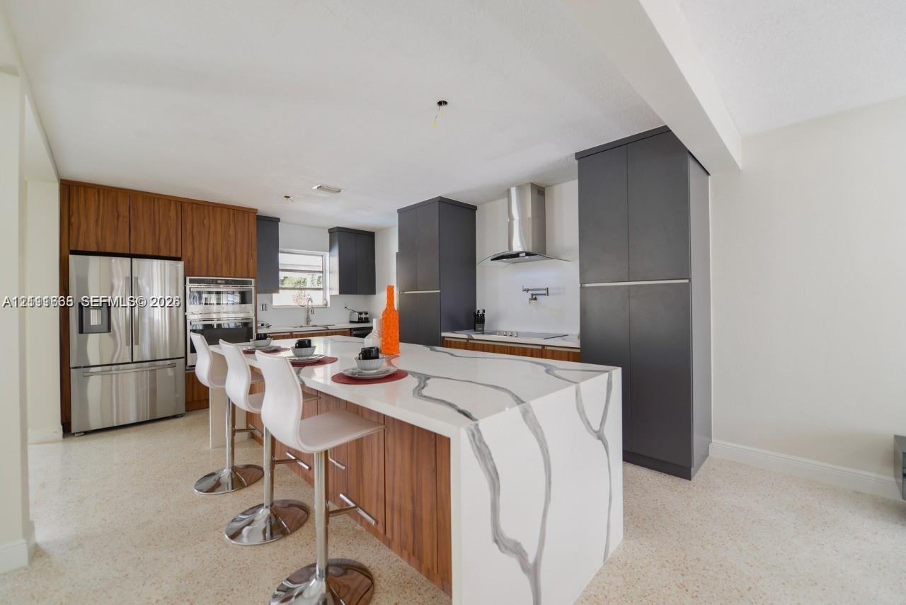 Kitchen featuring custom two-tone cabinetry, waterfall-edge stone island, built-in stainless steel appliances, and professional-grade range hood Kitchen featuring custom two-tone cabinetry, waterfall-edge stone island, built-in stainless steel appliances, and professional-grade range hood