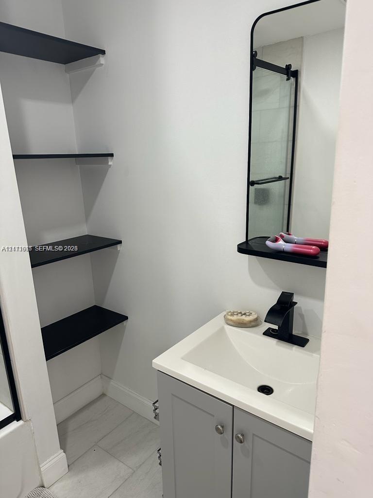 Built-in black shelving, modern vanity with white countertop, integrated sink, matte black faucet, and rectangular mirror with black frame