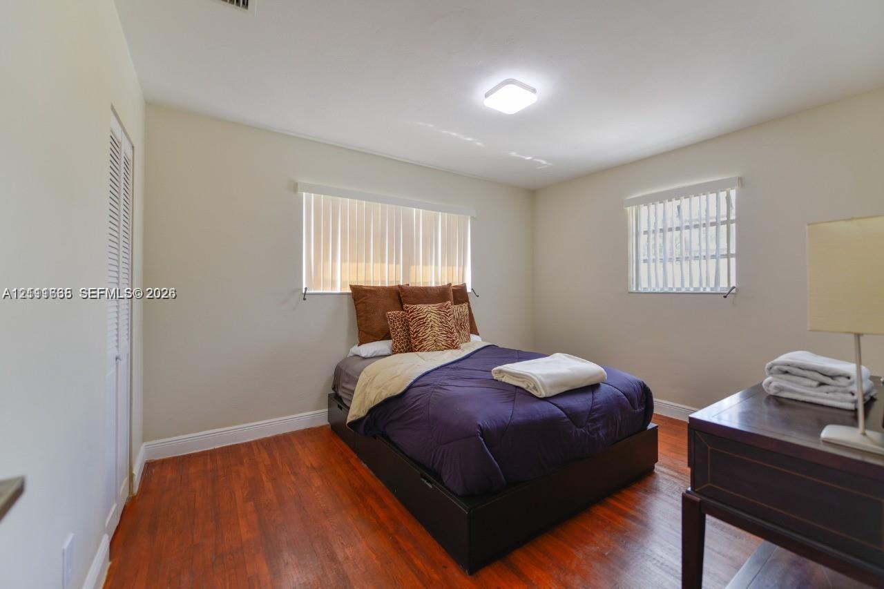 Room featuring wood-finish flooring, dual windows with vertical blinds, and a built-in closet with louvered doors
