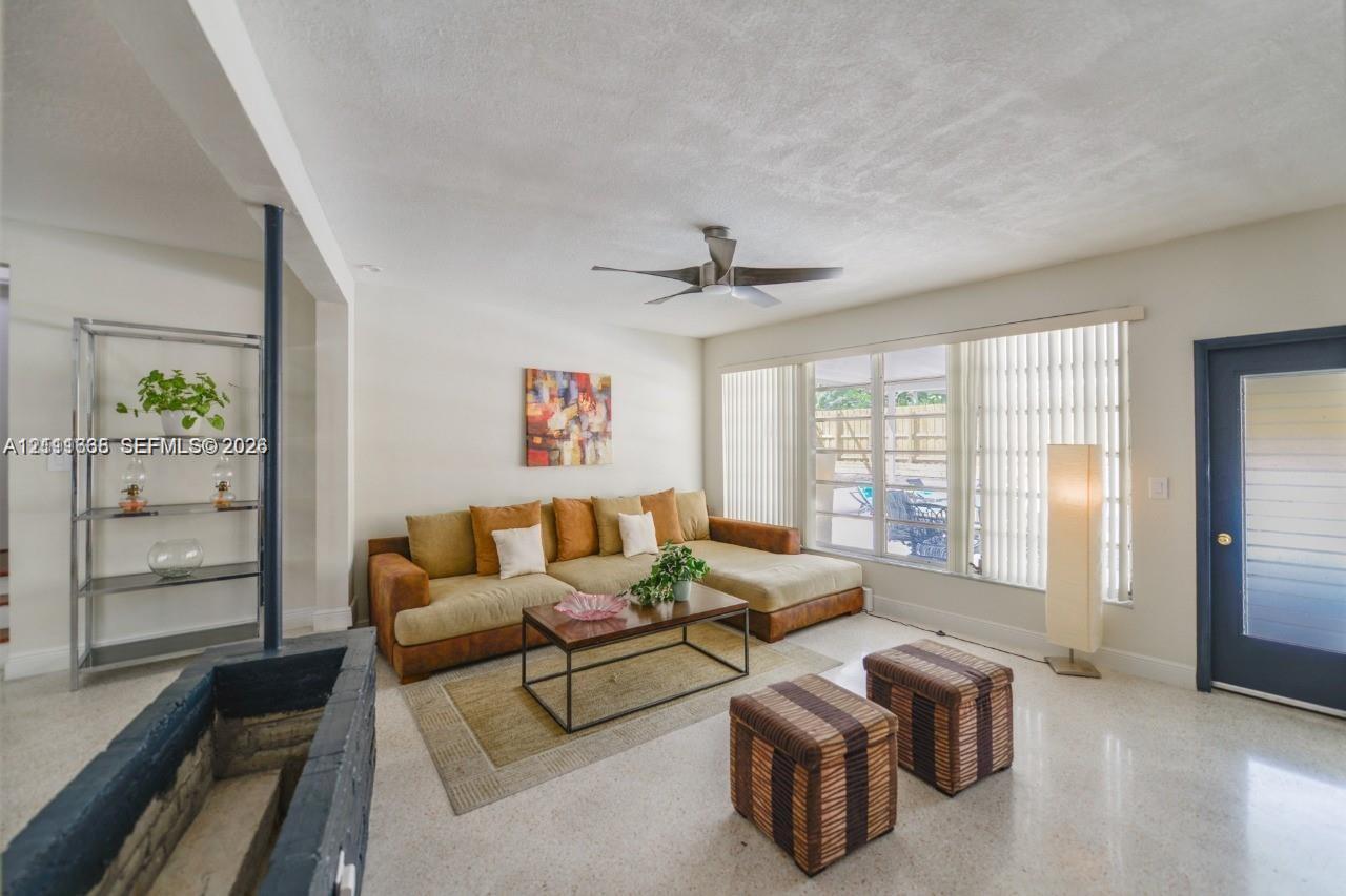 Living area featuring terrazzo flooring, a fireplace with a painted stone hearth, a central ceiling fan, and a glass-panel entry door