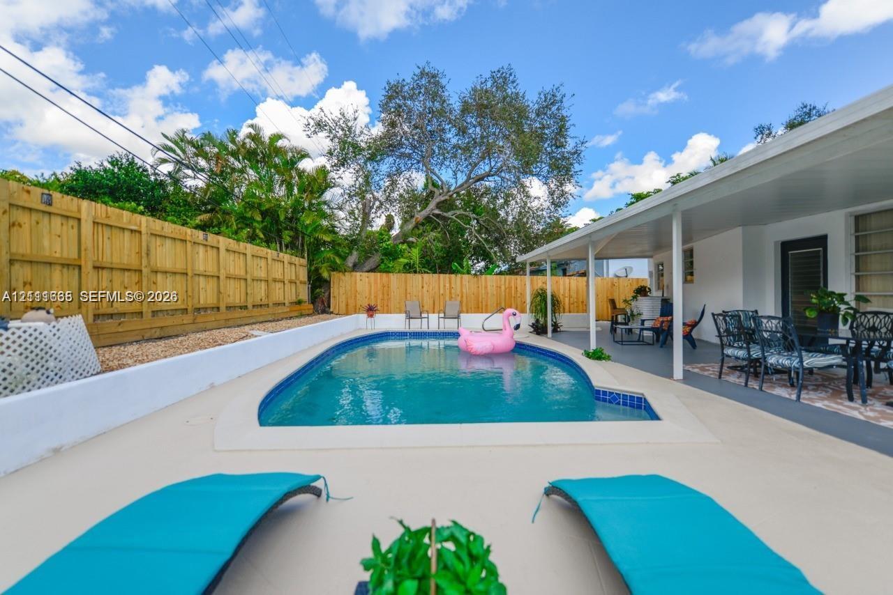 In-ground swimming pool with tile trim, expansive concrete deck, covered patio, and wood privacy fencing