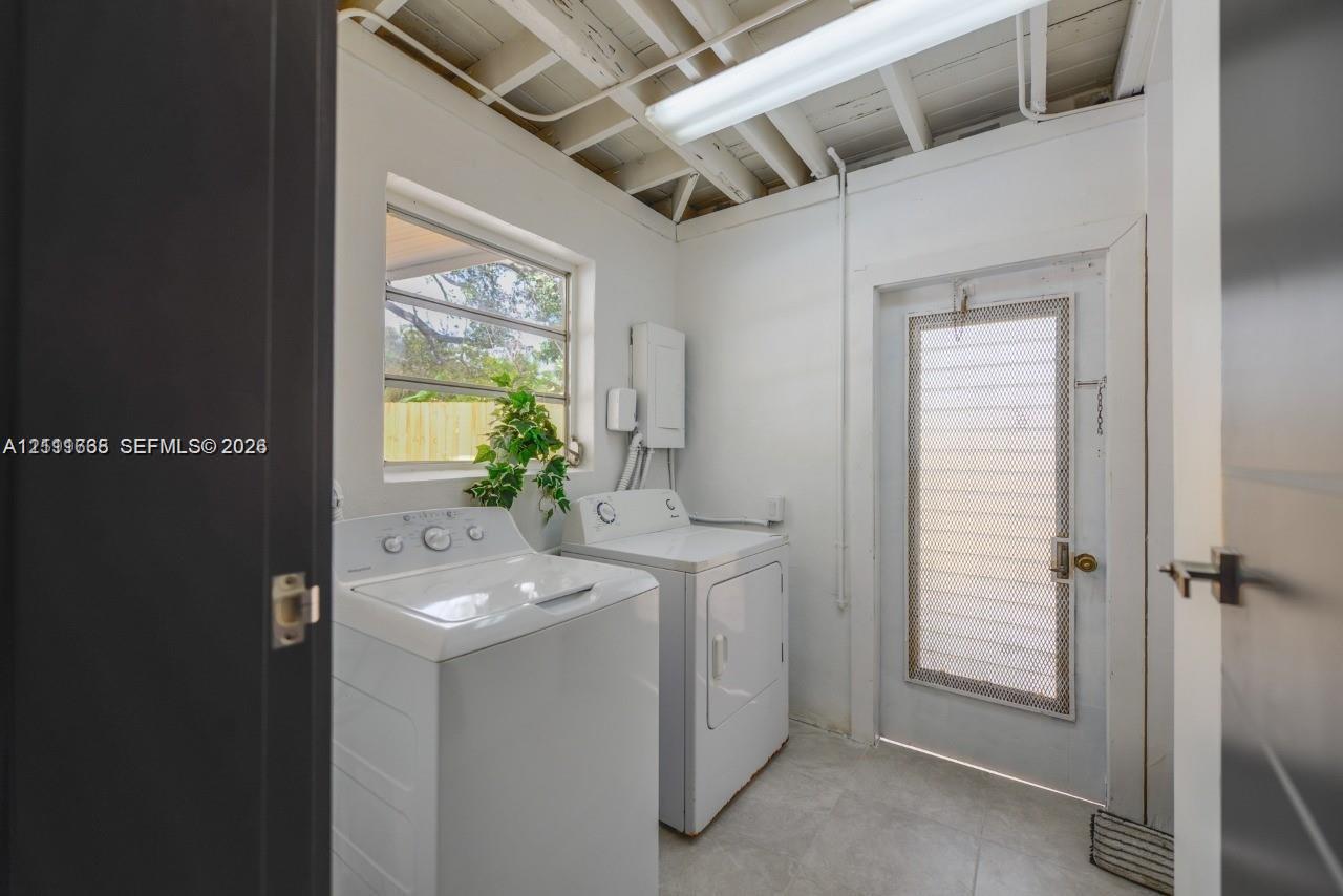 Utility room featuring exposed ceiling joists, tile flooring, a window, and an exterior door with integrated security screening