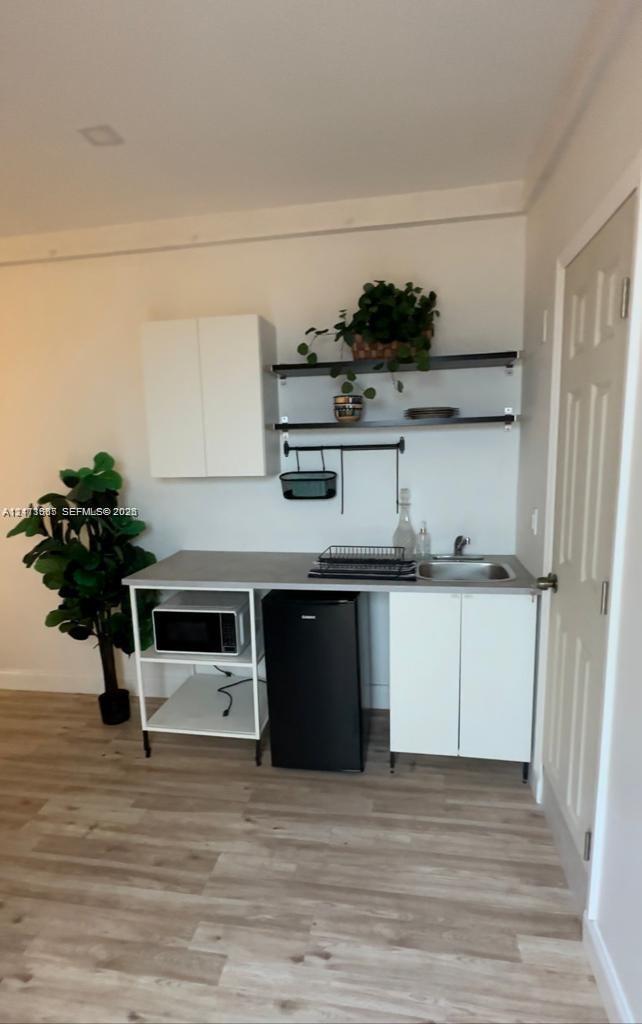 Kitchenette featuring white cabinetry, wood-finish flooring, a stainless steel sink with a metallic faucet, and open metal shelving