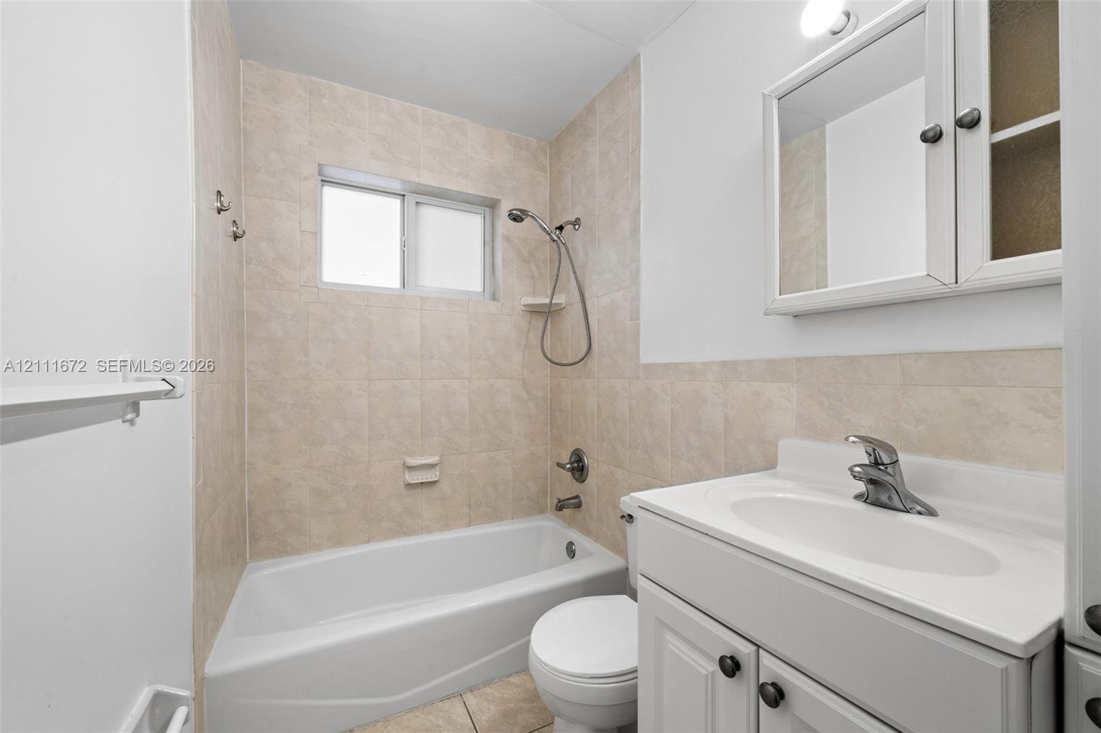 Bathroom featuring a white vanity cabinet with a stone-top integrated sink, ceramic tile tub surround, handheld shower fixture, and wall-mounted medicine cabinet