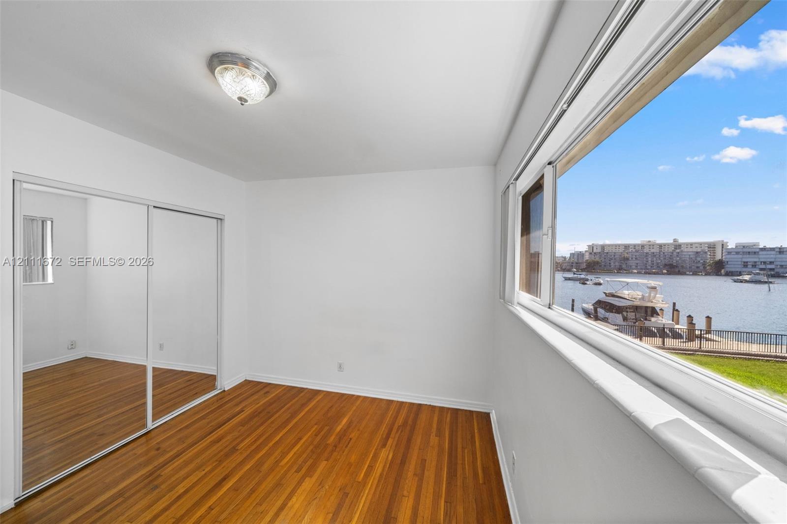Hardwood flooring, expansive window, mirrored sliding closet doors, flush-mount ceiling light, and water backdrop