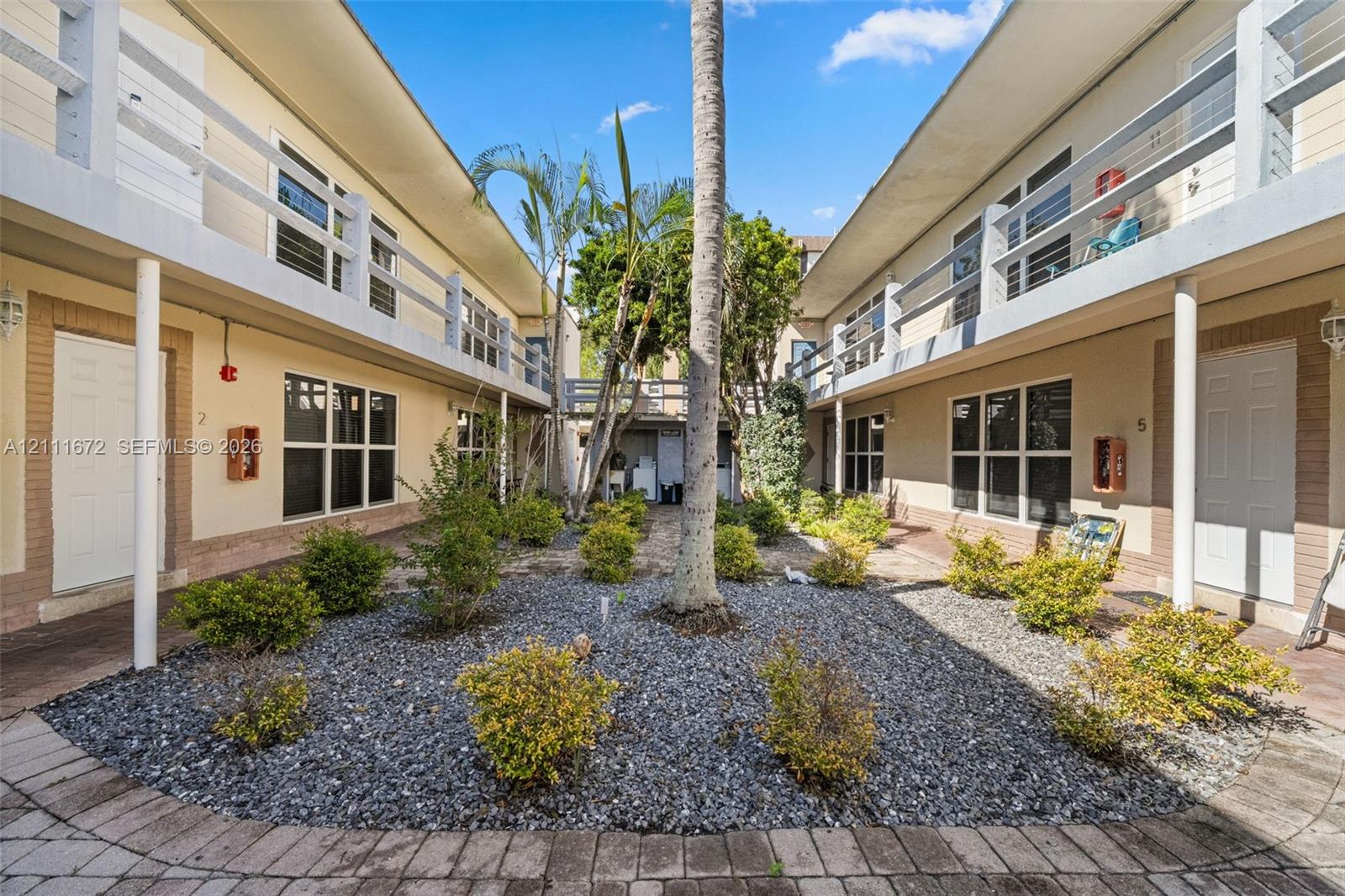 Central courtyard featuring gravel landscaping, mature palm trees, multi-level railed walkways, and paver-edged pathways Central courtyard featuring gravel landscaping, mature palm trees, multi-level railed walkways, and paver-edged pathways