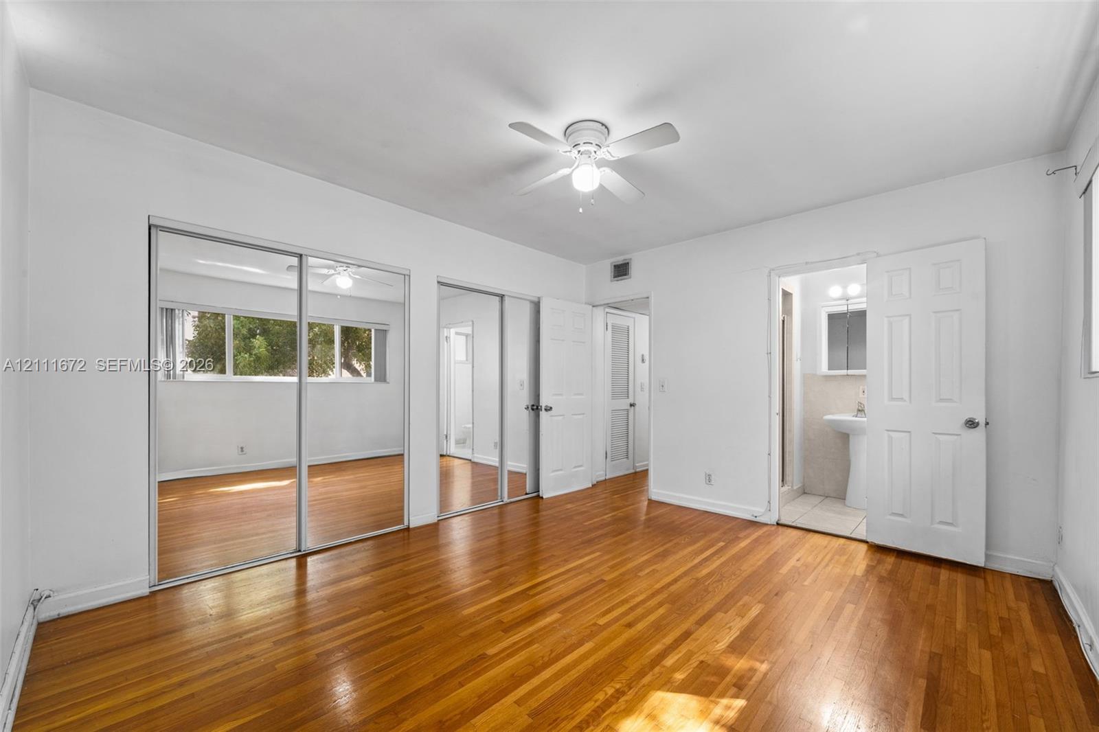 Wood-finish flooring, dual sliding mirrored closet doors, white panel doors, and a ceiling-mounted light fixture