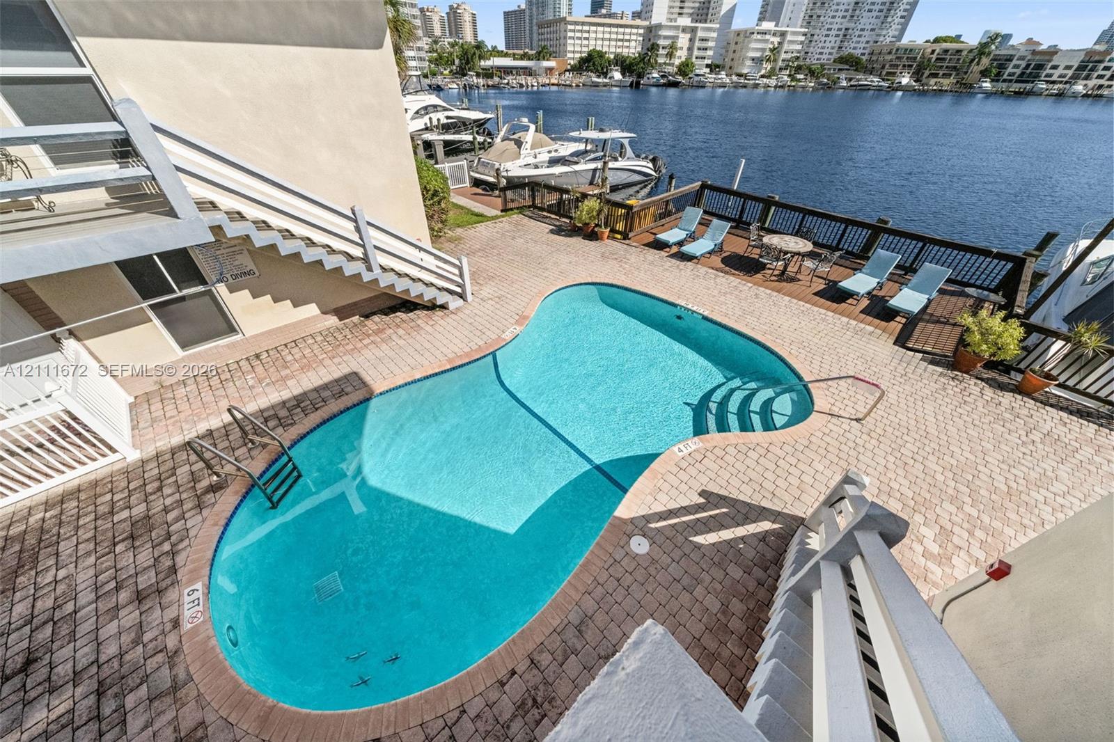 Waterfront patio featuring a kidney-shaped pool, paver hardscaping, a wooden bulkhead, and metal railings