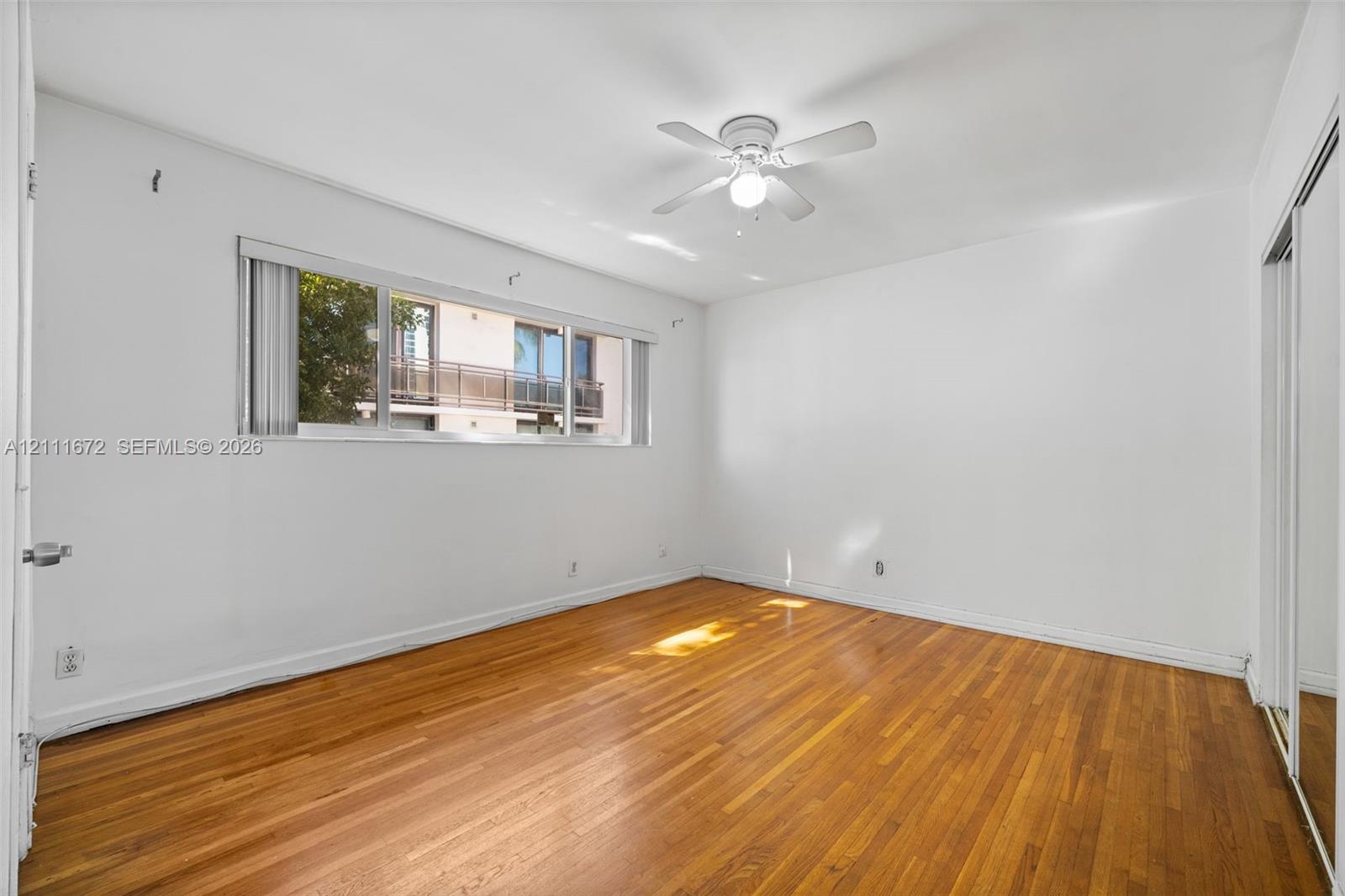 Interior space featuring wood-finish flooring, a horizontal sliding window, a ceiling-mounted light fixture with a fan, and mirrored sliding closet doors