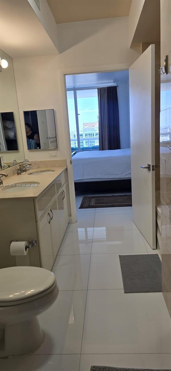 Bathroom featuring a dual-sink vanity with light-toned countertop, large wall-mounted mirror, and polished tile flooring