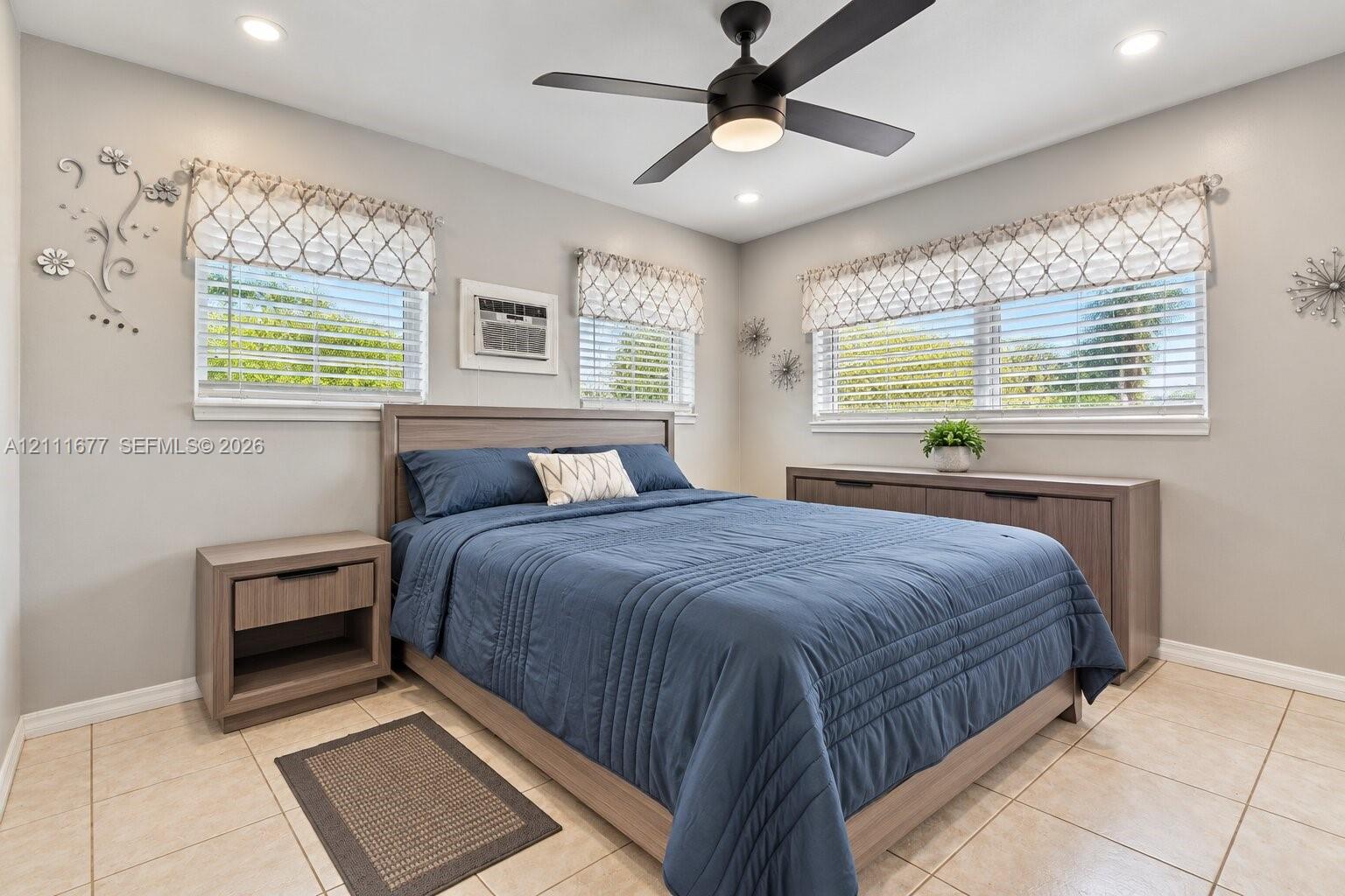 Neutral-toned room featuring large-format tile flooring, recessed ceiling lighting, and a dark-finish ceiling fan with an integrated light fixture