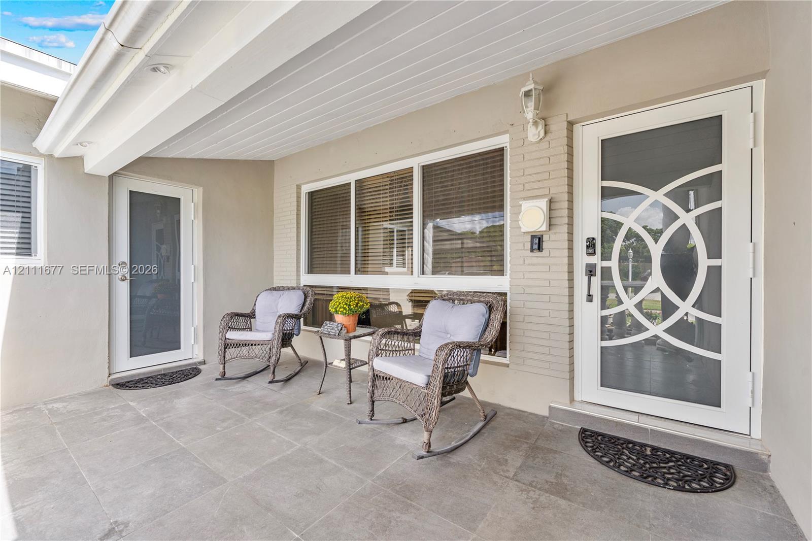 Covered porch featuring large-format tile flooring, white brick accents, and two exterior doors with decorative circular-patterned glass inserts Covered porch featuring large-format tile flooring, white brick accents, and two exterior doors with decorative circular-patterned glass inserts
