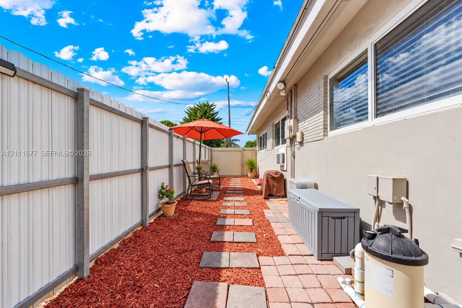 Side yard featuring a perimeter metal privacy fence, red mulch ground cover, and square concrete paver pathway