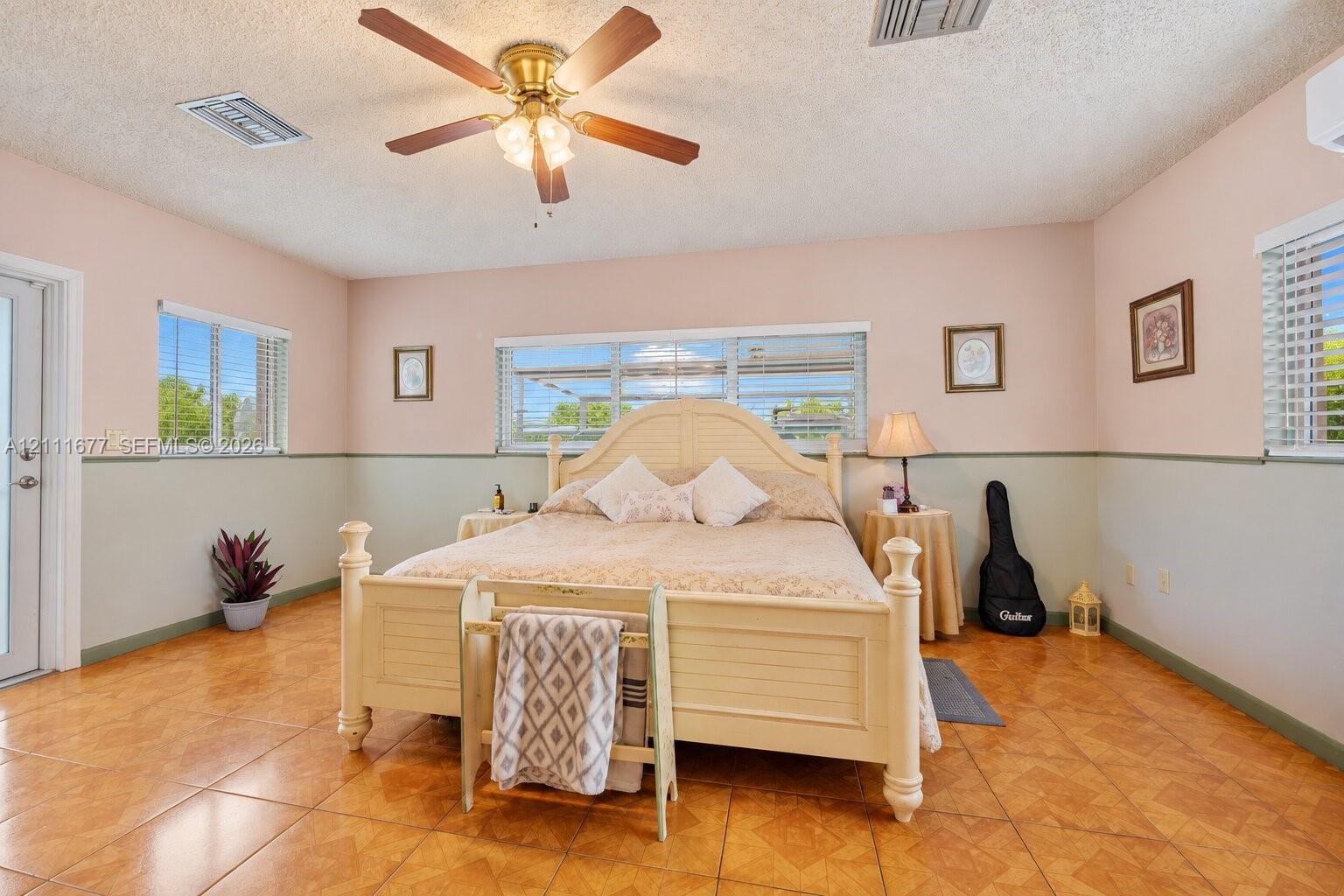 Spacious room featuring large-format ceramic tile flooring, neutral wall paneling with a chair rail, multi-pane windows, and a ceiling fan with integrated lighting
