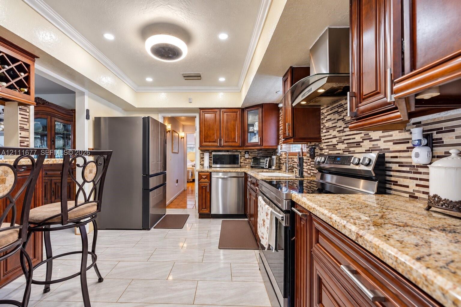 Kitchen featuring wood cabinetry, stone countertops, stainless steel appliances, multi-tonal backsplash, and tile flooring