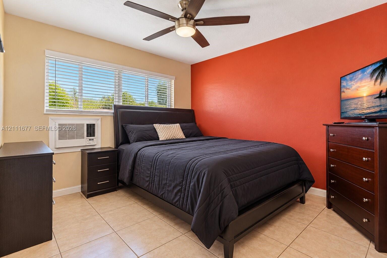 Neutral-toned tile flooring, large windows with horizontal blinds, integrated air conditioning unit, and a ceiling fan with light fixture