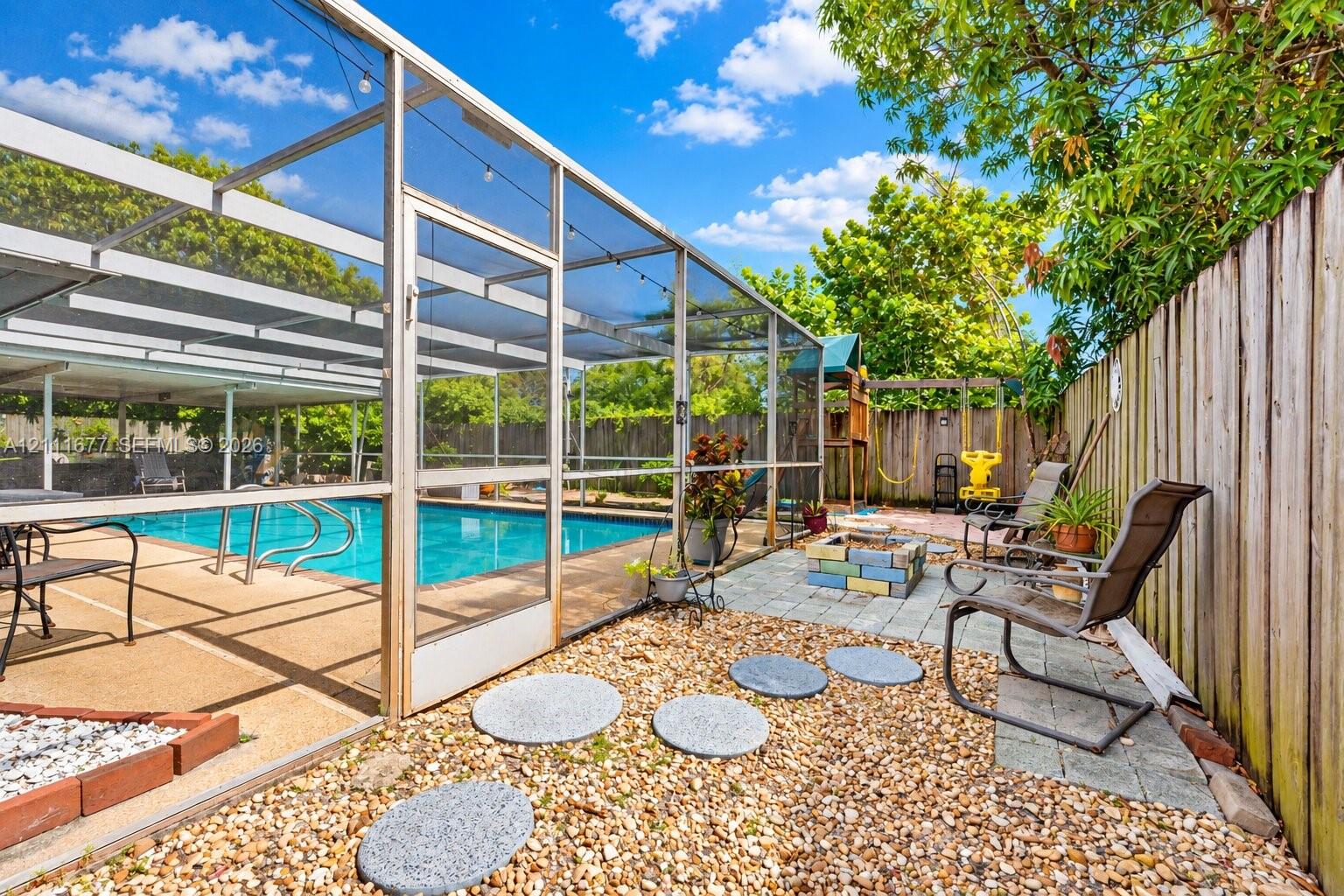 Screen-enclosed swimming pool featuring a concrete deck and a stone paver patio area with a built-in fire pit