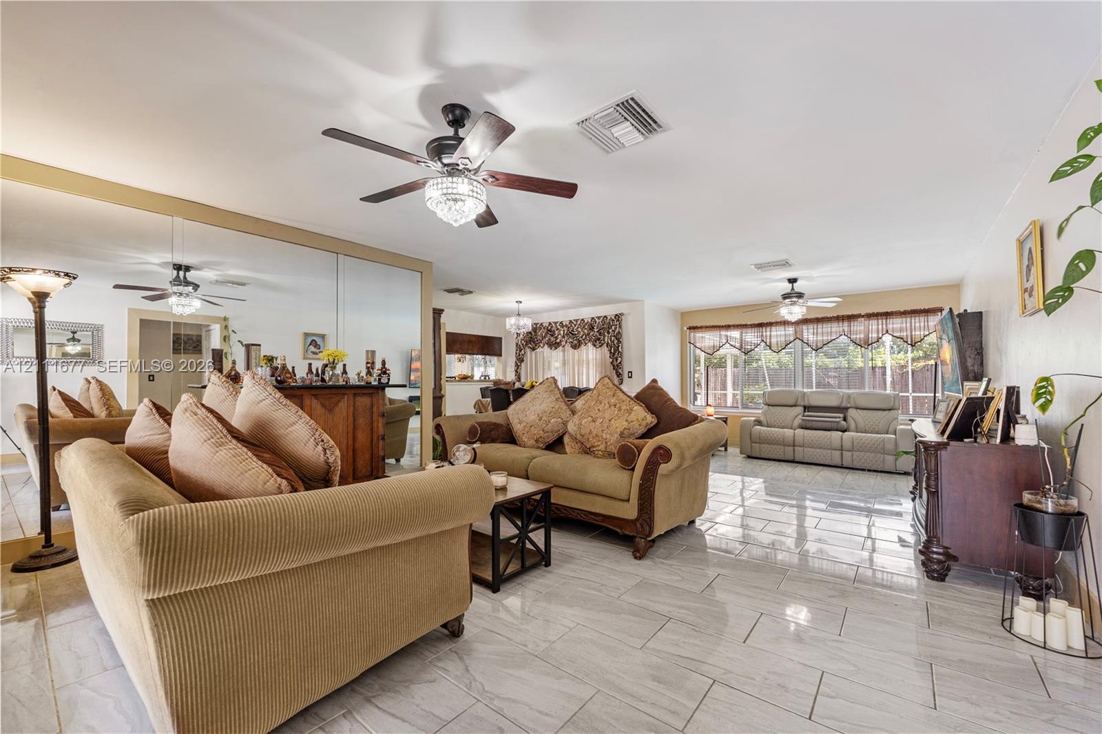 Spacious living area featuring polished tile flooring, wall-to-wall mirrored accent, and two ceiling fans with integrated lighting fixtures