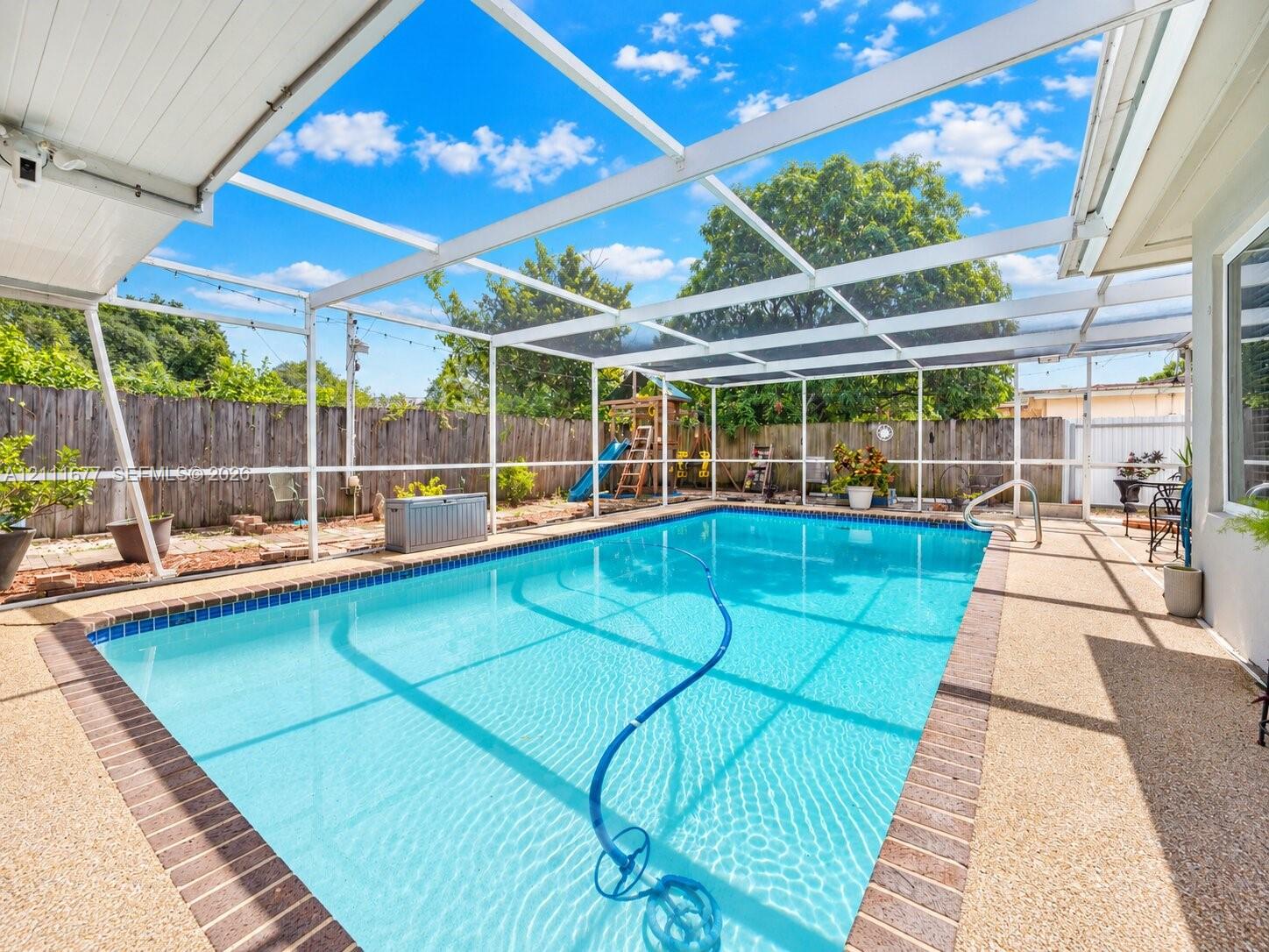 In-ground swimming pool with brick paver coping and screened-in enclosure, featuring an exposed aggregate pool deck and perimeter wood privacy fencing In-ground swimming pool with brick paver coping and screened-in enclosure, featuring an exposed aggregate pool deck and perimeter wood privacy fencing