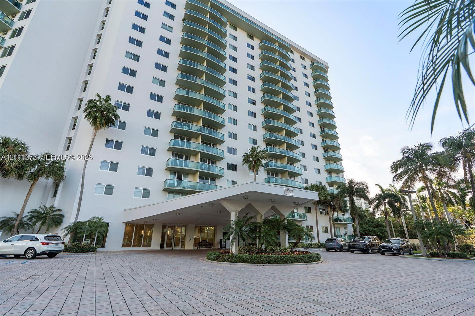 High-rise exterior featuring a tiered faade with private glass-railed balconies, a covered porte-cochre entry, and a paved arrival plaza with circular landscaping