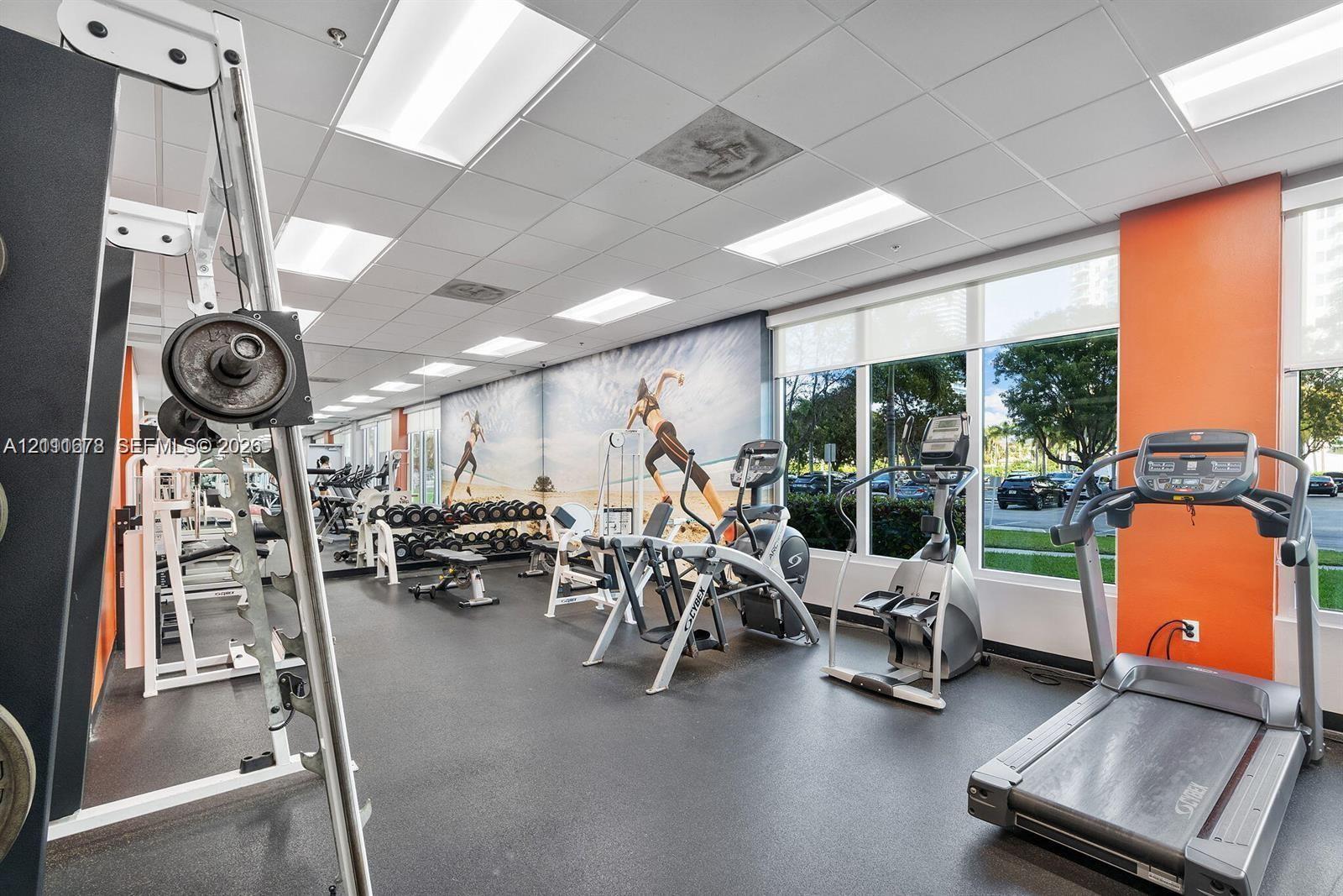 Fitness center featuring rubber flooring, drop ceiling with recessed lighting, large-scale wall-to-wall mirrors, and floor-to-ceiling windows