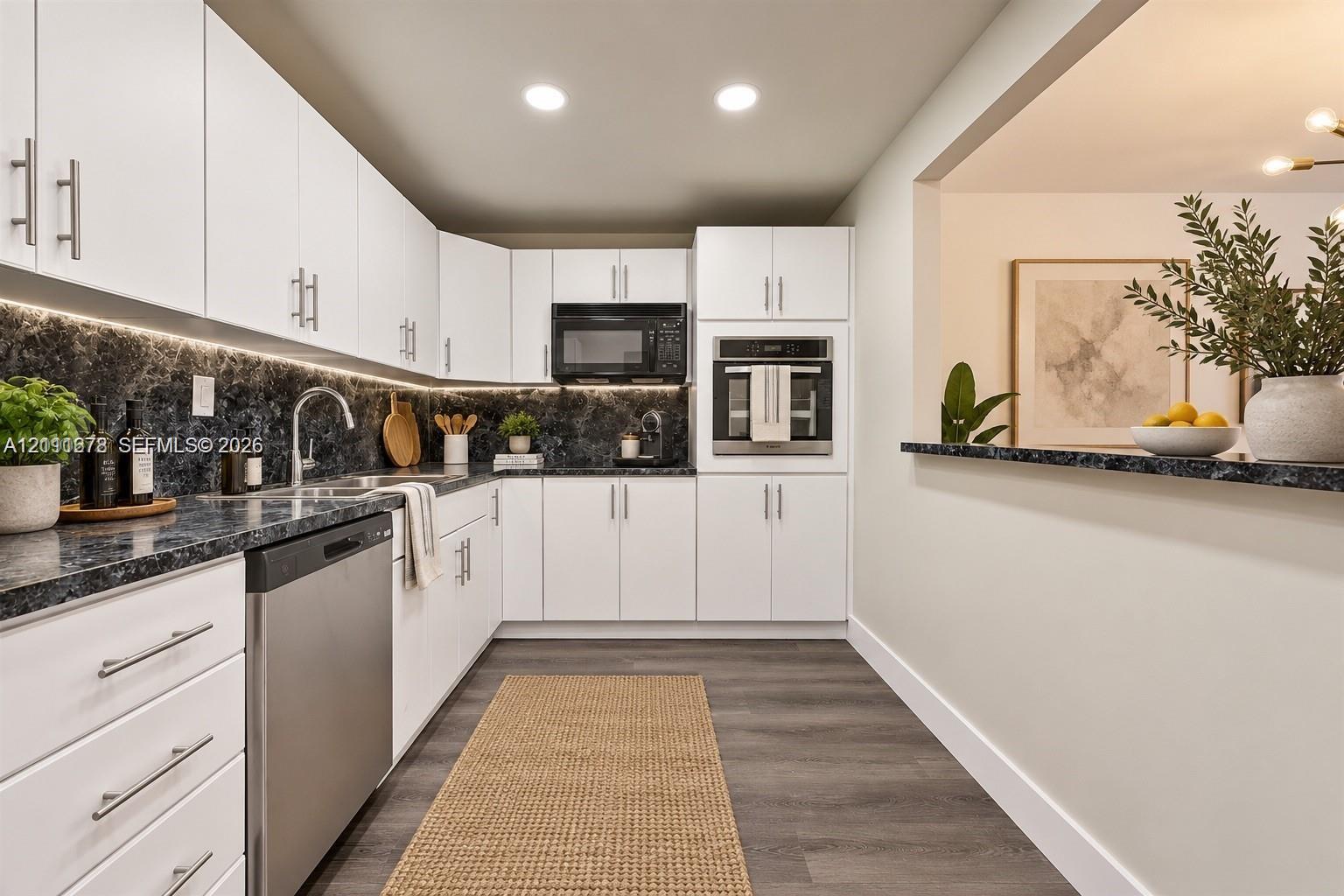 White shaker-style cabinetry, dark stone-finish countertops, stainless steel appliances, integrated under-cabinet lighting, and wood-finish flooring