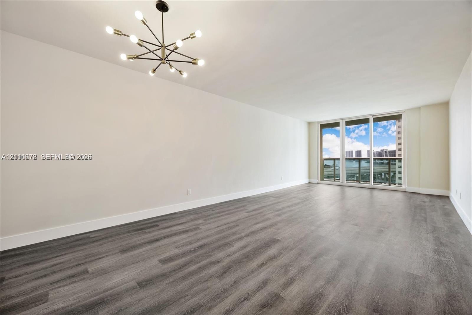 Spacious room featuring wood-finish flooring, a modern sputnik-style chandelier, and floor-to-ceiling glass paneling with an exterior balcony