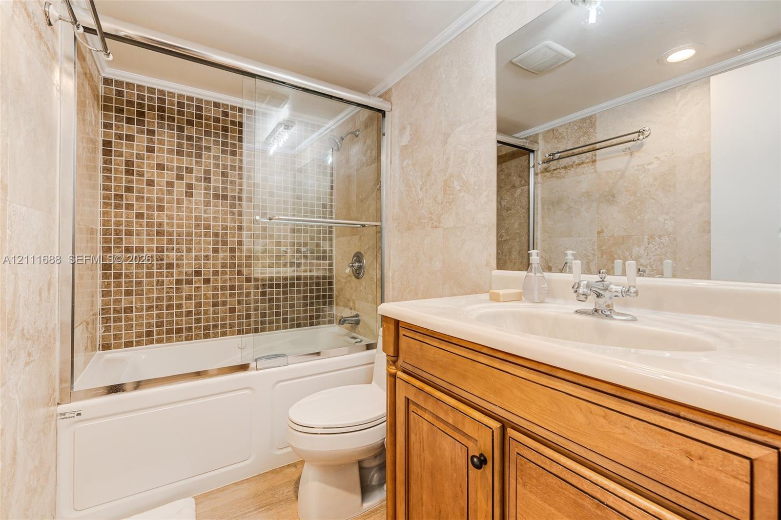 Bathroom featuring stone wall tiling, wood-finish vanity with an integrated countertop sink, mosaic tile shower surround, glass shower enclosure, and chrome faucet hardware