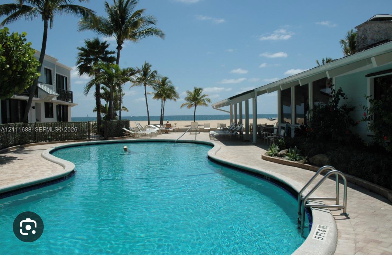 Curvilinear swimming pool with stone paver decking, sheltered patio, and oceanfront placement Curvilinear swimming pool with stone paver decking, sheltered patio, and oceanfront placement