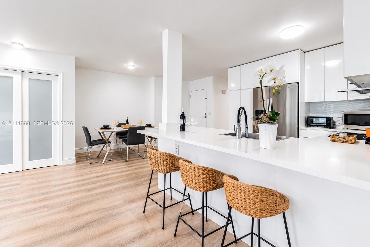 Kitchen featuring high-gloss white cabinetry, quartz countertops, stainless steel appliances, a peninsula with integrated sink, and wood-finish flooring