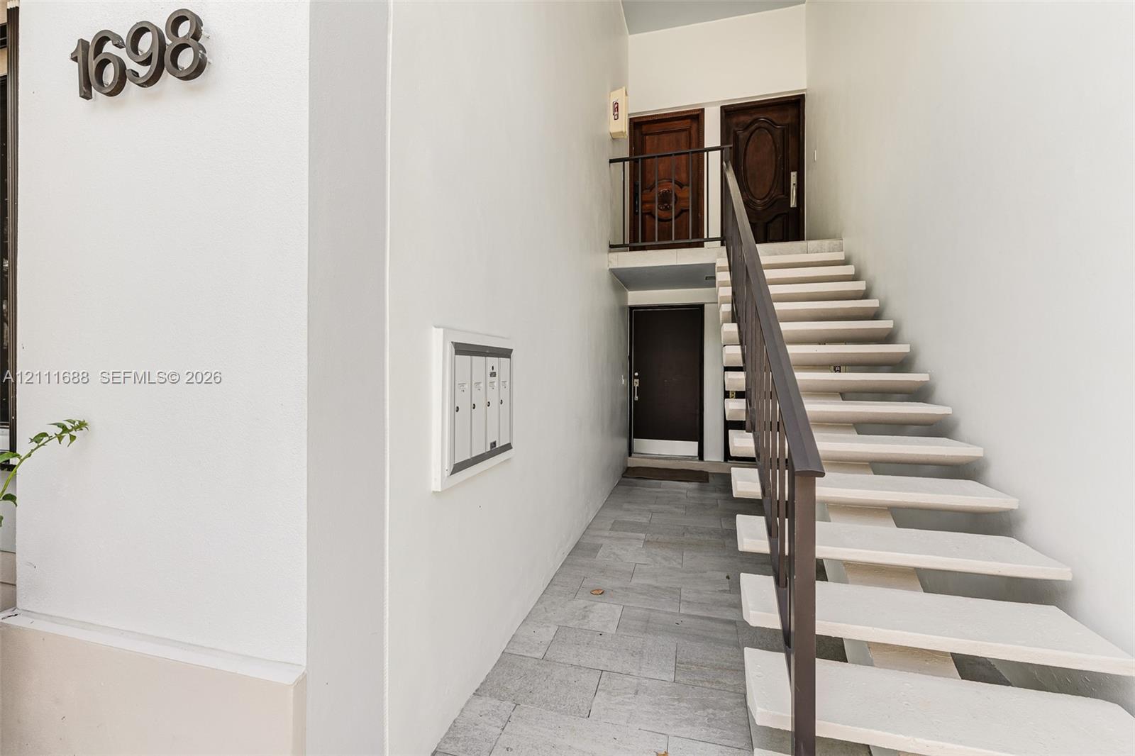 Exterior entryway featuring stone-finish flooring, a metal staircase with a matching handrail, and multiple wood-panel entry doors Exterior entryway featuring stone-finish flooring, a metal staircase with a matching handrail, and multiple wood-panel entry doors