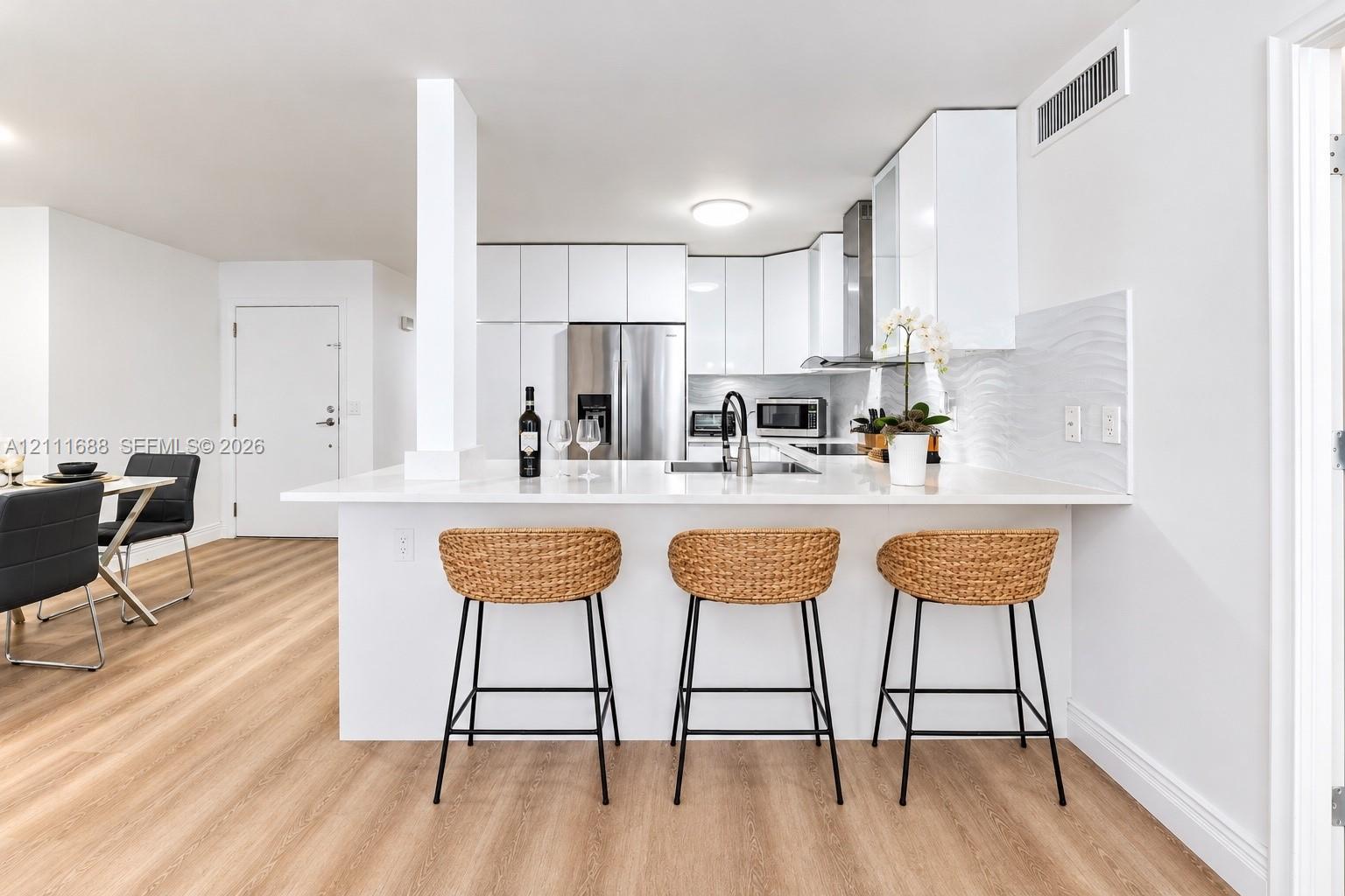 Kitchen featuring flat-panel white cabinetry, white stone-finish countertops, stainless steel appliances, textured tile backsplash, and light wood-finish flooring