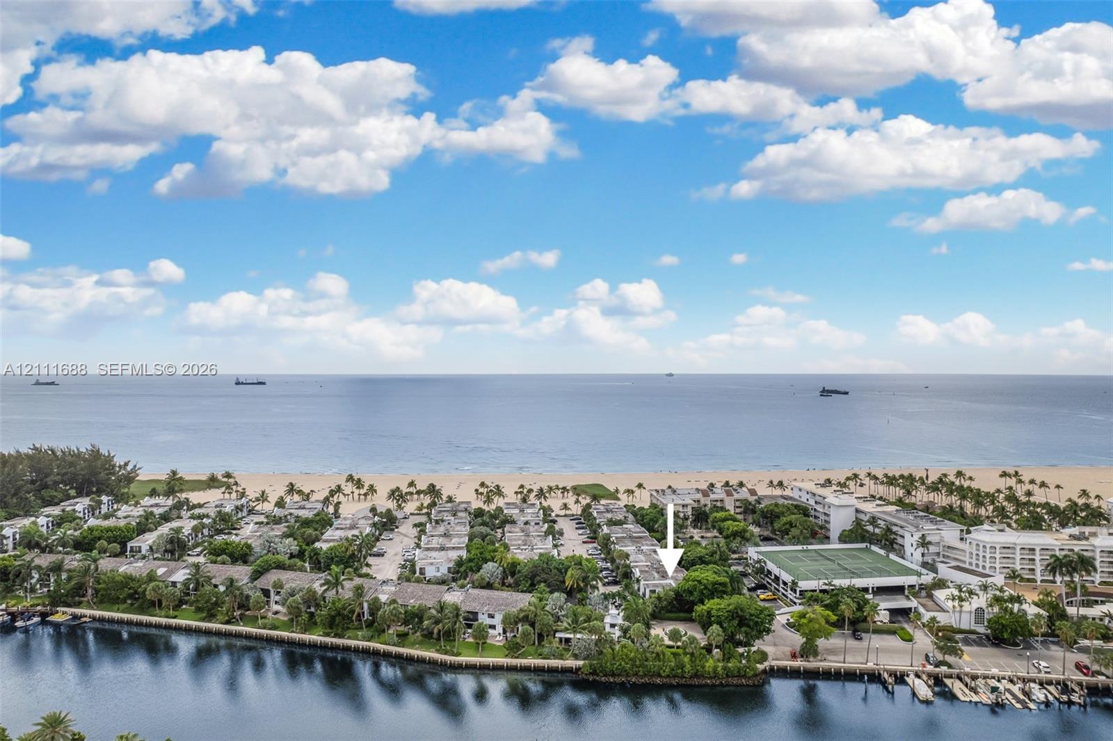Aerial perspective of waterfront property featuring proximity to the ocean, mature landscaping, and tennis court facilities