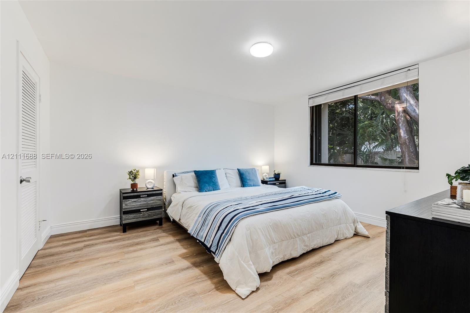Room featuring wood-finish flooring, a large window with exterior tree-lined scenery, and louvered closet doors