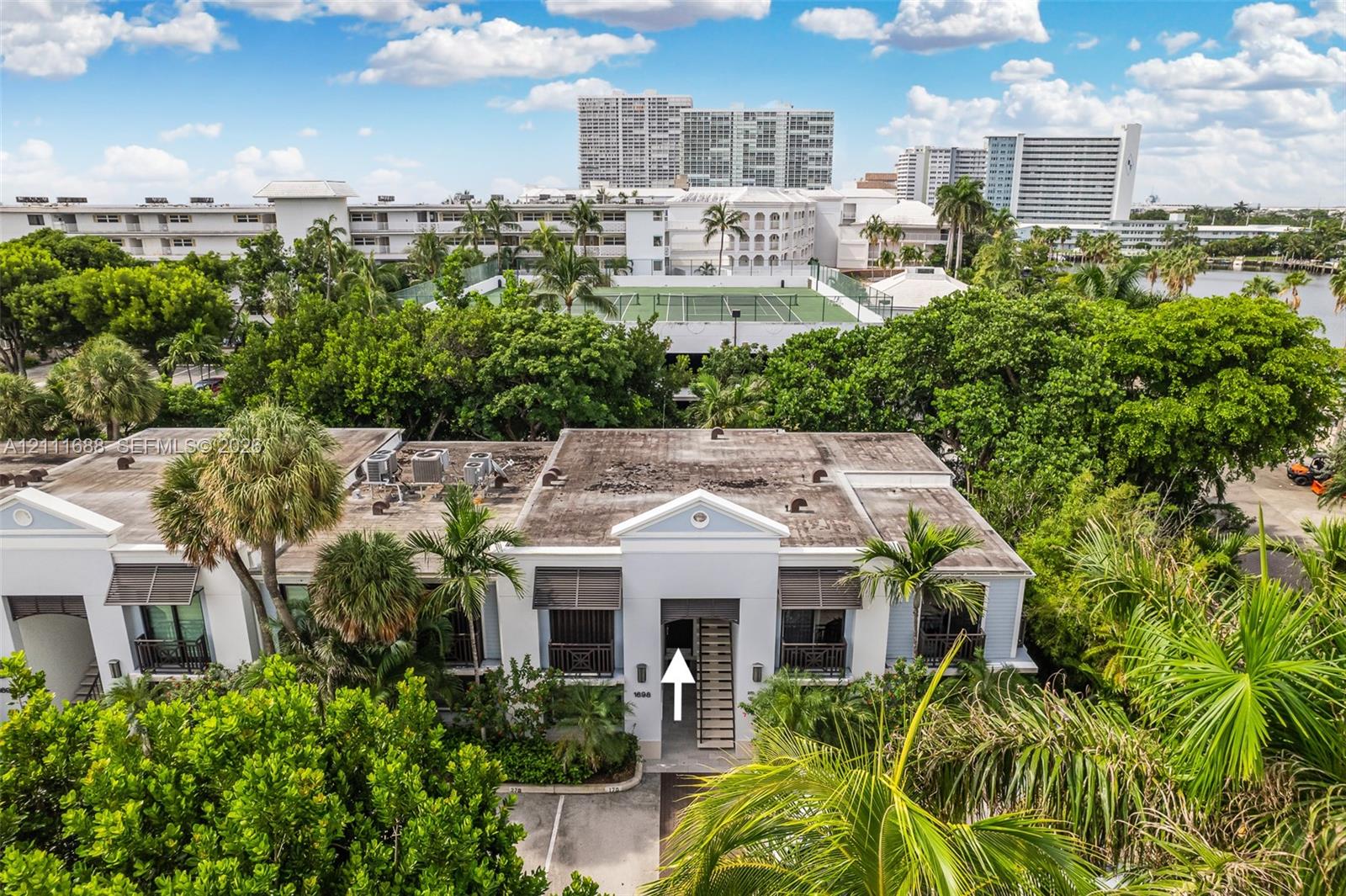 Multi-story building featuring a white facade, gabled entry detailing, metal window awnings, and mature palm tree landscaping Multi-story building featuring a white facade, gabled entry detailing, metal window awnings, and mature palm tree landscaping