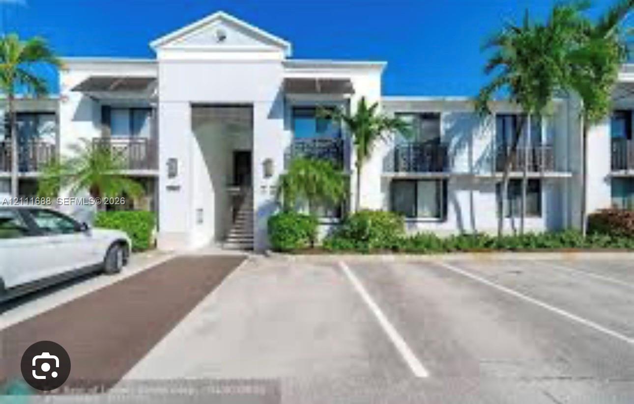 Stucco exterior facade featuring a central gabled entryway, second-story balconies with decorative railings, and manicured tropical landscaping Stucco exterior facade featuring a central gabled entryway, second-story balconies with decorative railings, and manicured tropical landscaping