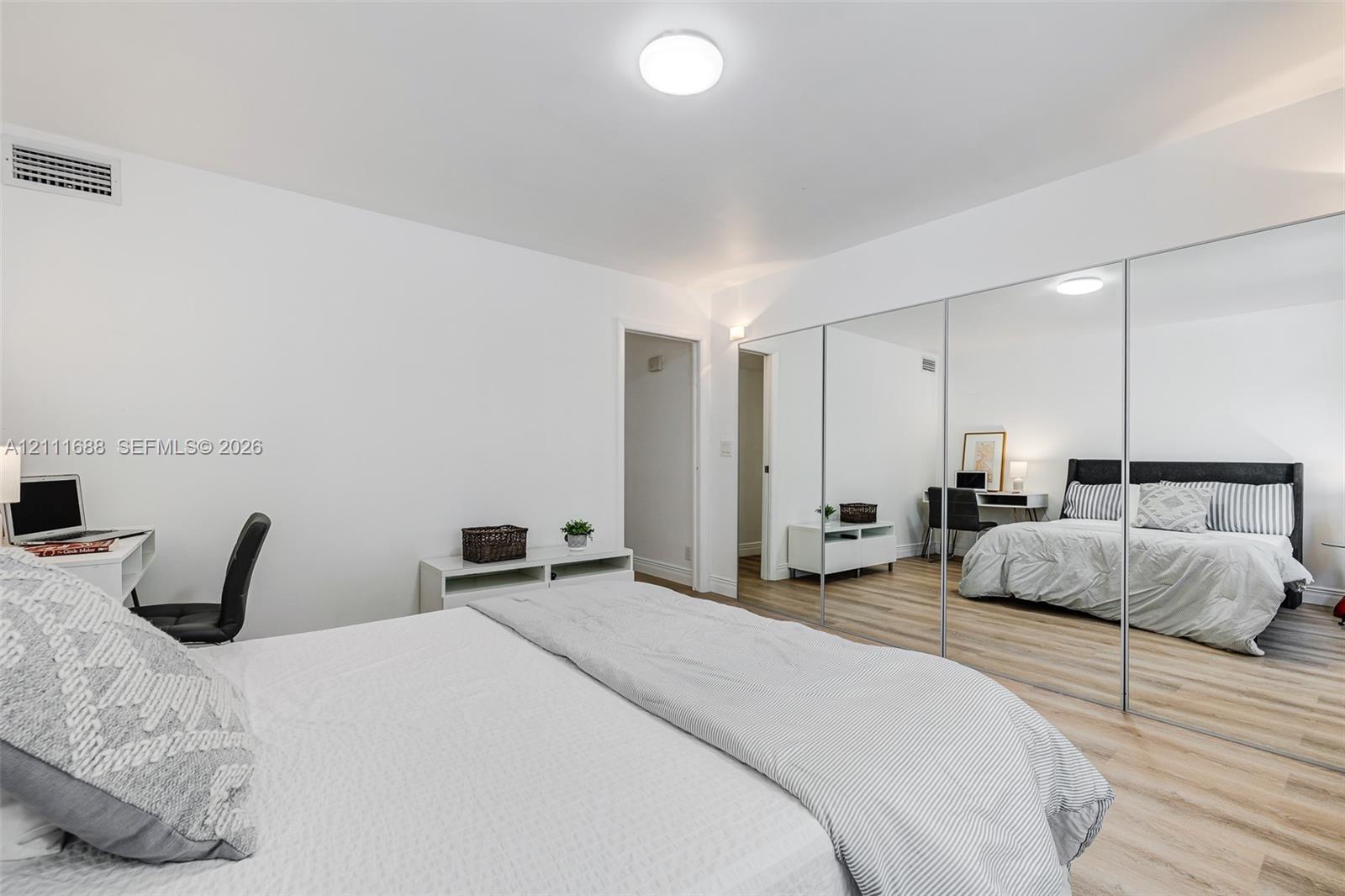 Room featuring wood-finish flooring, ceiling-mounted lighting, and a full-length mirrored sliding door closet