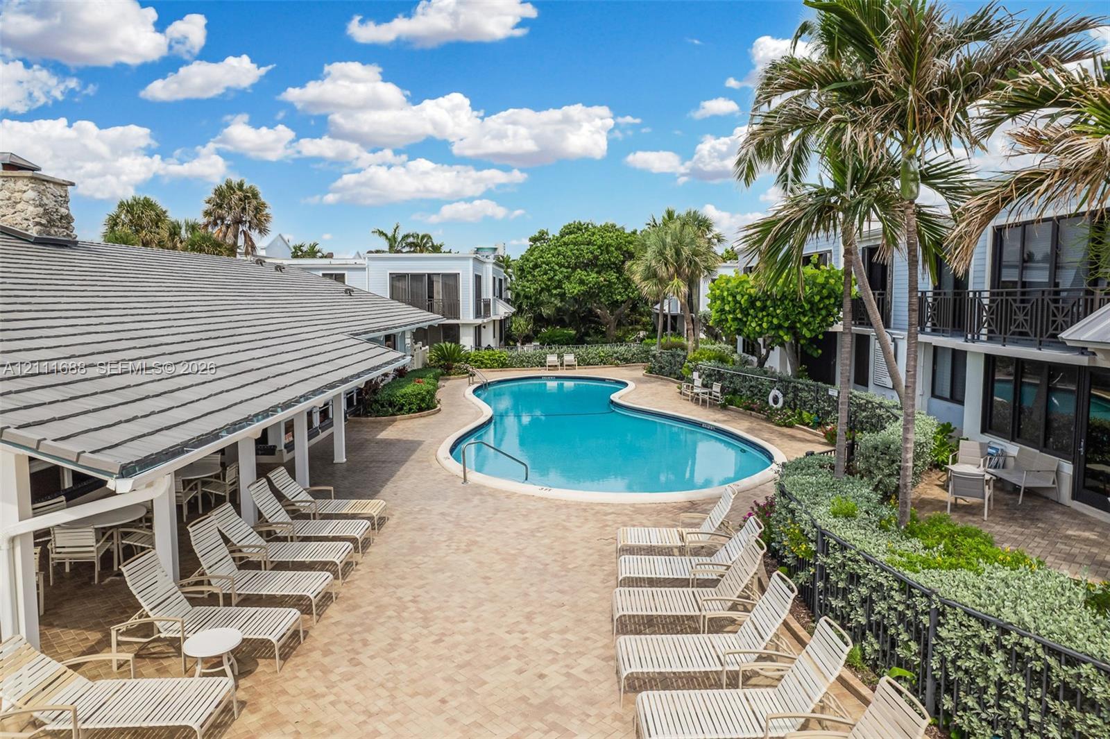 Curved swimming pool featuring a concrete paver pool deck and a covered patio area with support columns