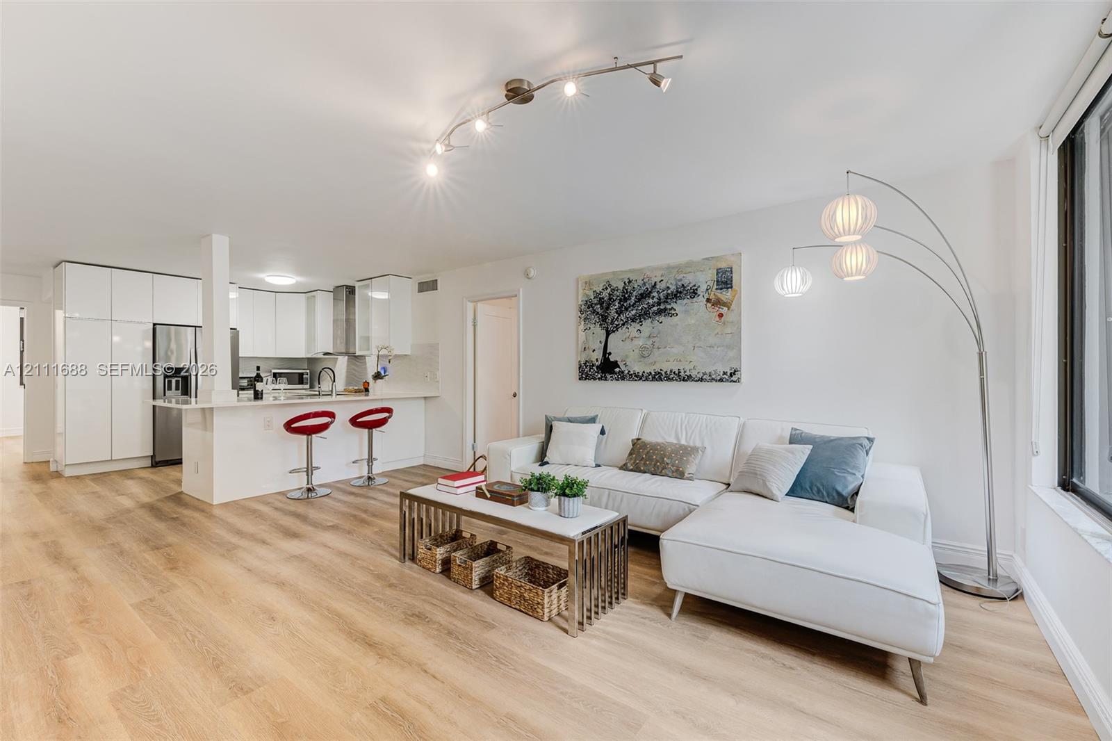 Open-concept interior featuring light wood-finish flooring, white flat-panel cabinetry, a peninsula with stone-finish countertop, and multi-directional track lighting