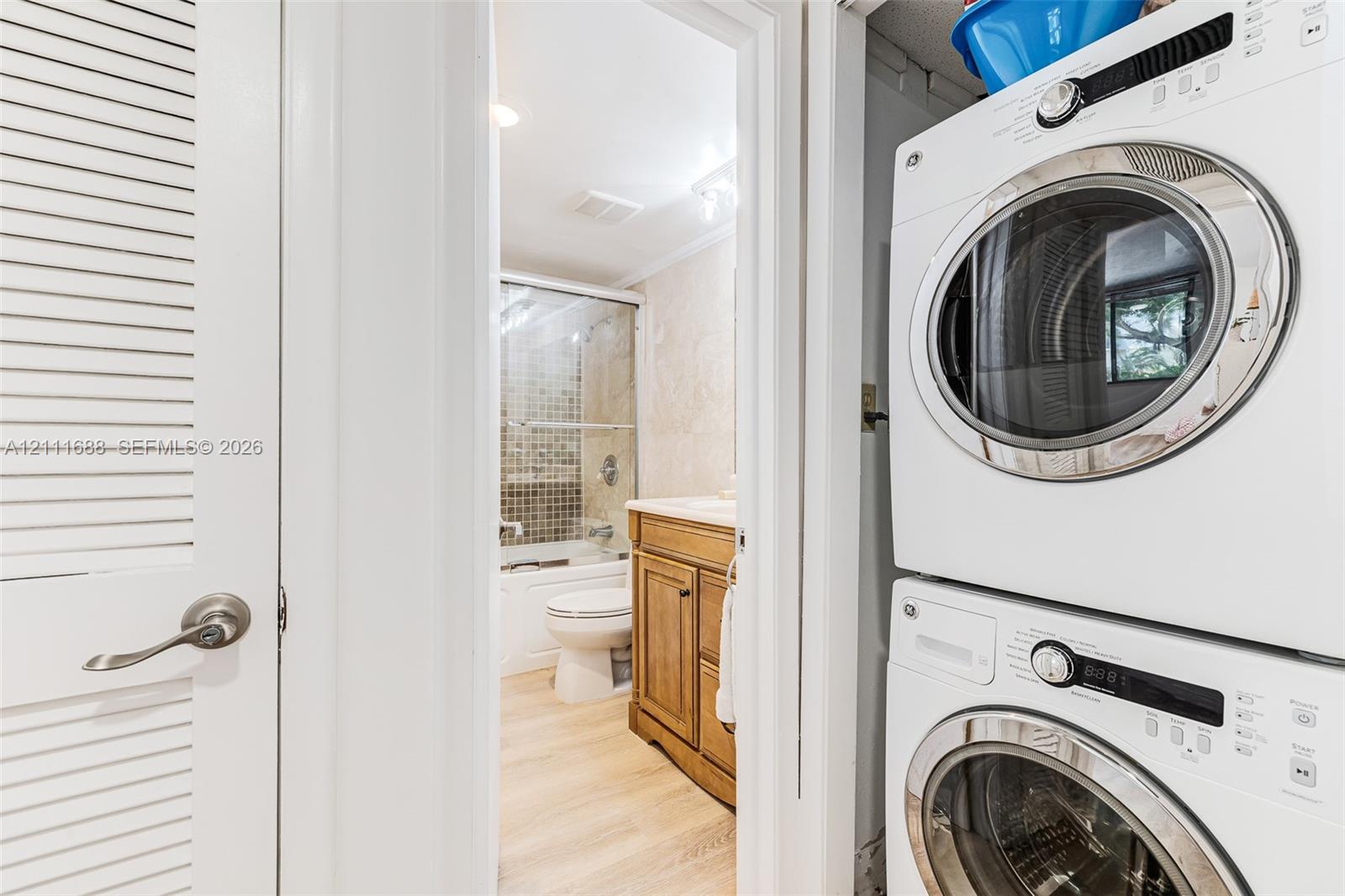 Laundry area featuring a stacked washer and dryer unit, louvered closet door, and wood-finish flooring
