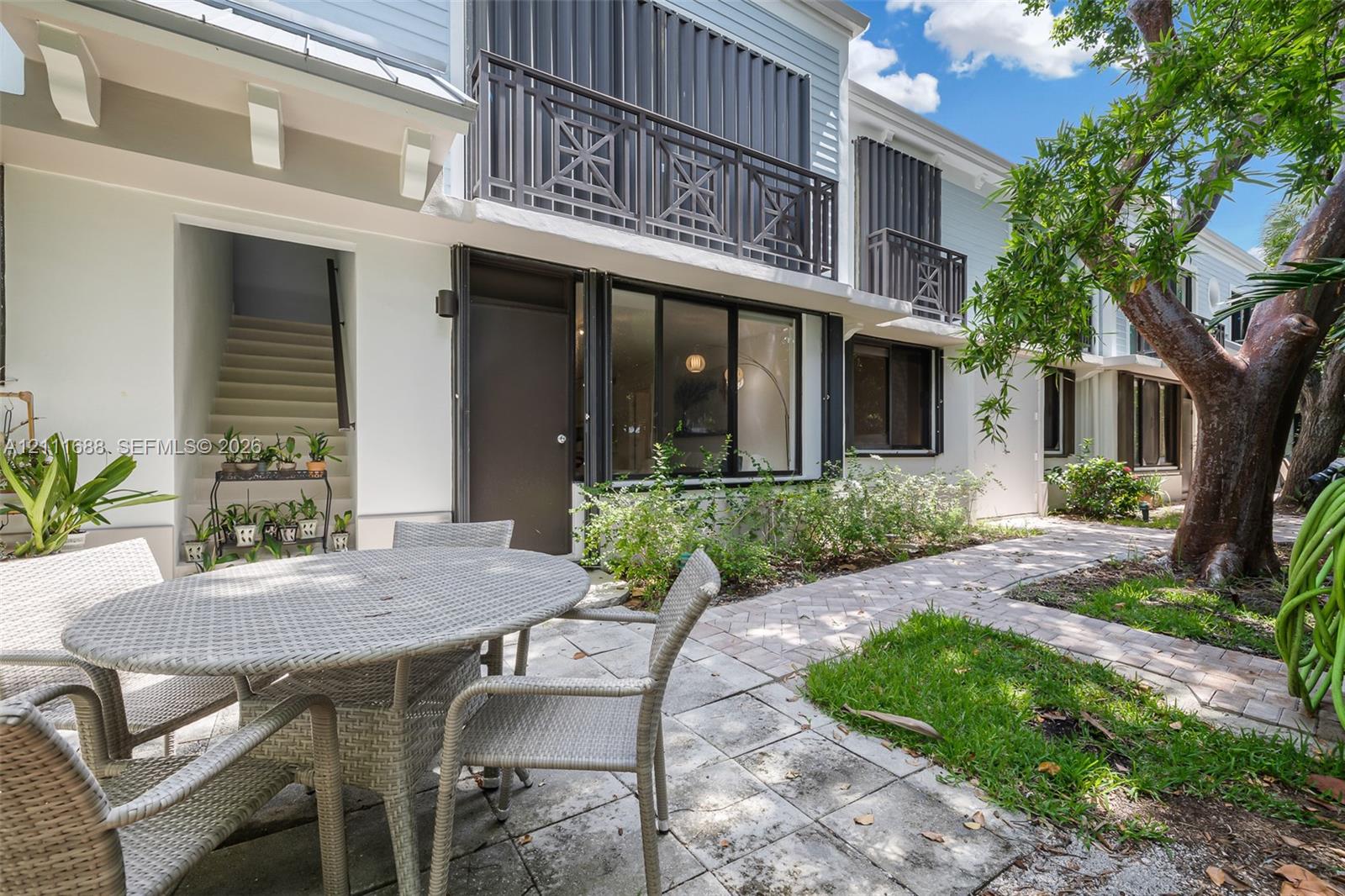 Exterior patio featuring paved hardscaping, second-story balconies with geometric metal railings, and horizontal lap siding