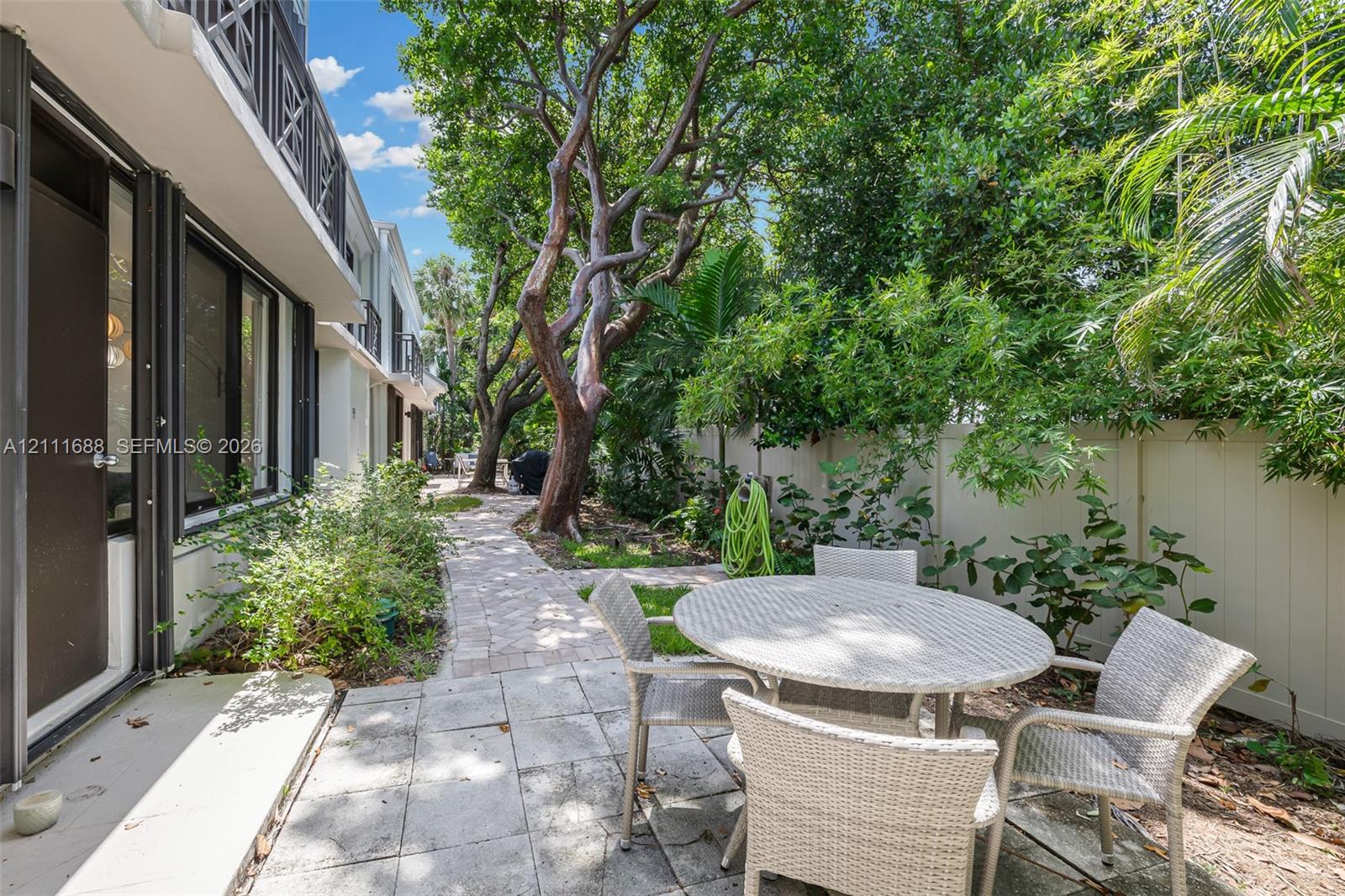 Private outdoor space featuring stone paver hardscaping, mature trees, ornamental landscaping, and a solid perimeter privacy fence