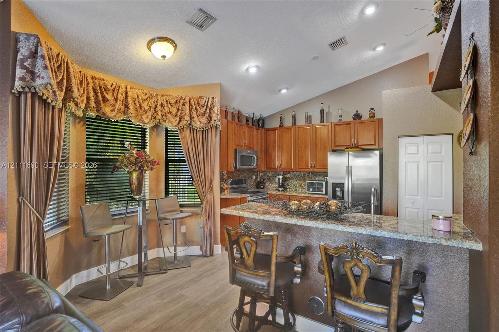Kitchen featuring wood cabinetry, stone-surface breakfast bar, recessed lighting, and bay windows