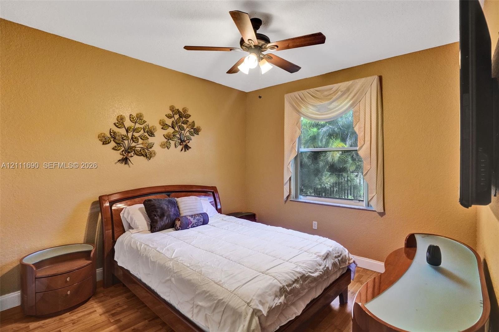 Room featuring wood-finish flooring, a ceiling fan with integrated lighting, and a window with exterior greenery