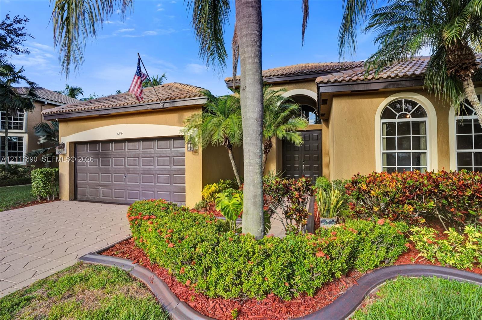 Stucco exterior featuring arched windows, a tiled roof, a paver driveway, and a paneled garage door