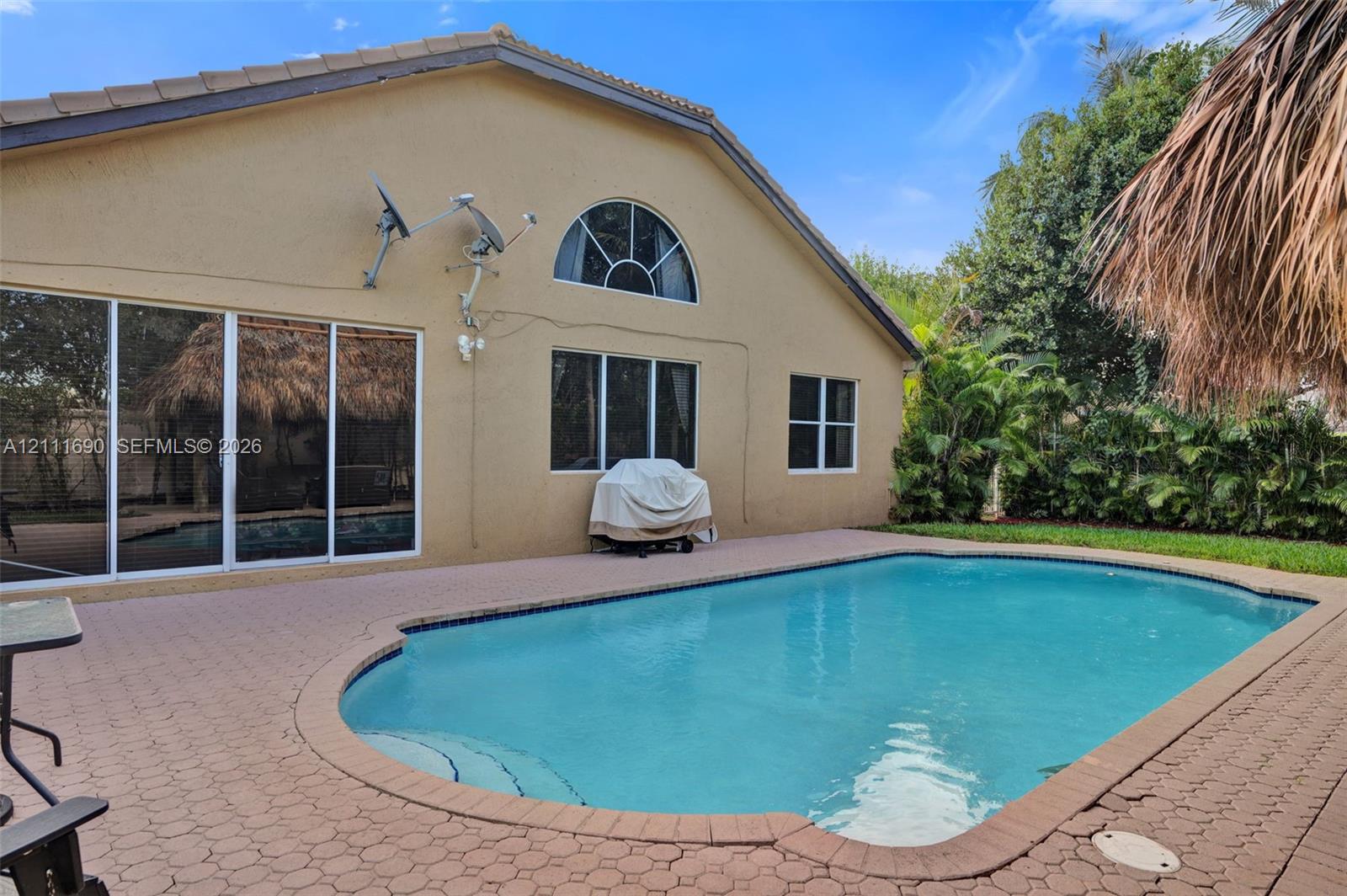 Stucco exterior featuring a large arched window, sliding glass doors, a concrete paver patio, and an inground swimming pool