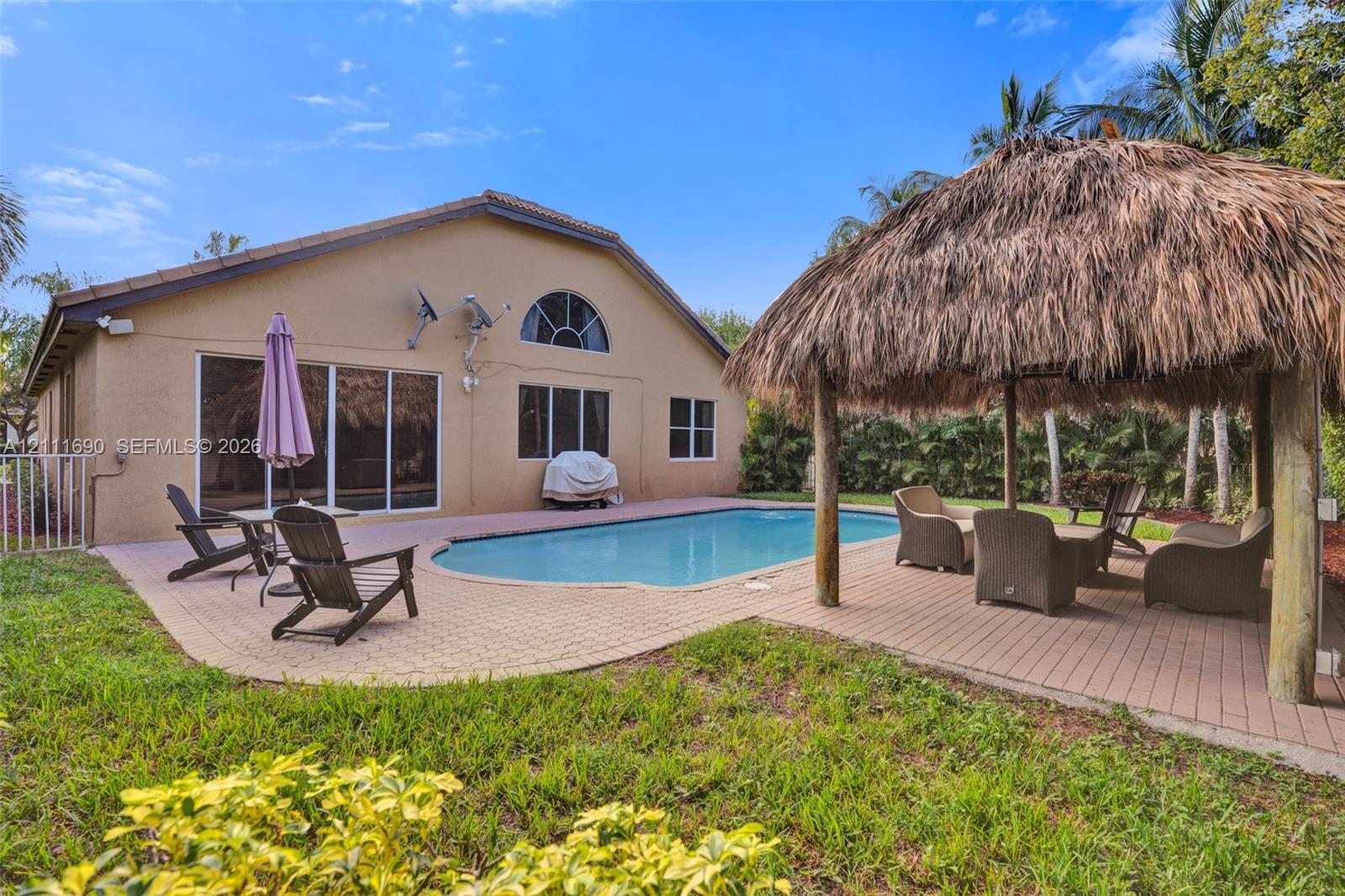 Rear exterior featuring a swimming pool, brick paver patio, and a thatched-roof tiki hut structure